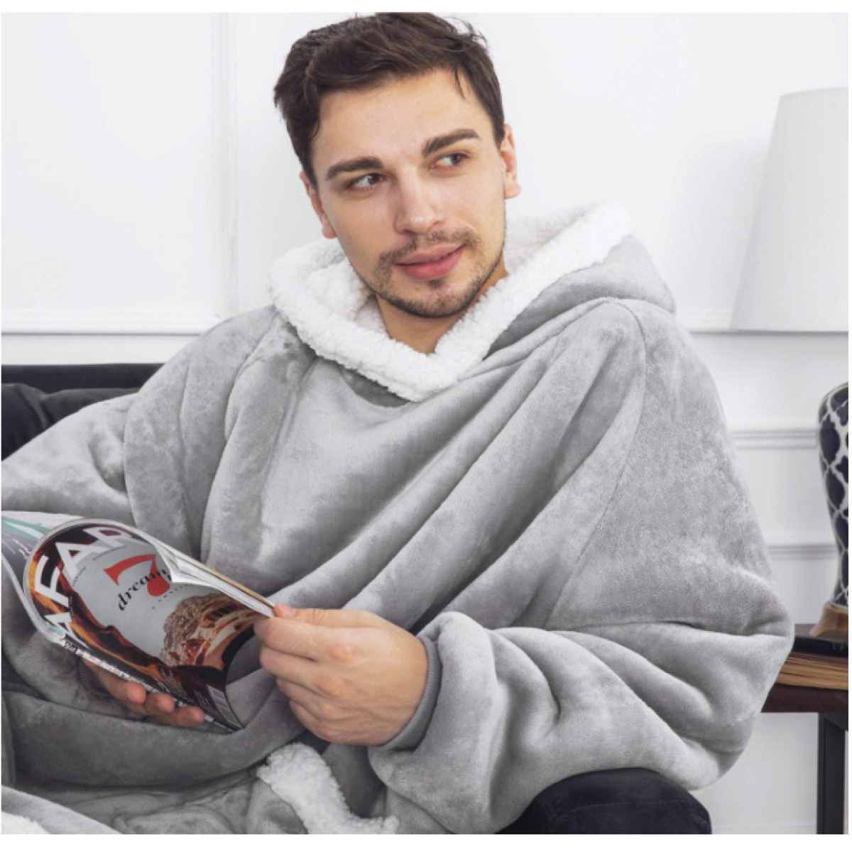 Ein Mann in grauer Kapuzendecke liest auf dem Sofa ein Magazin.