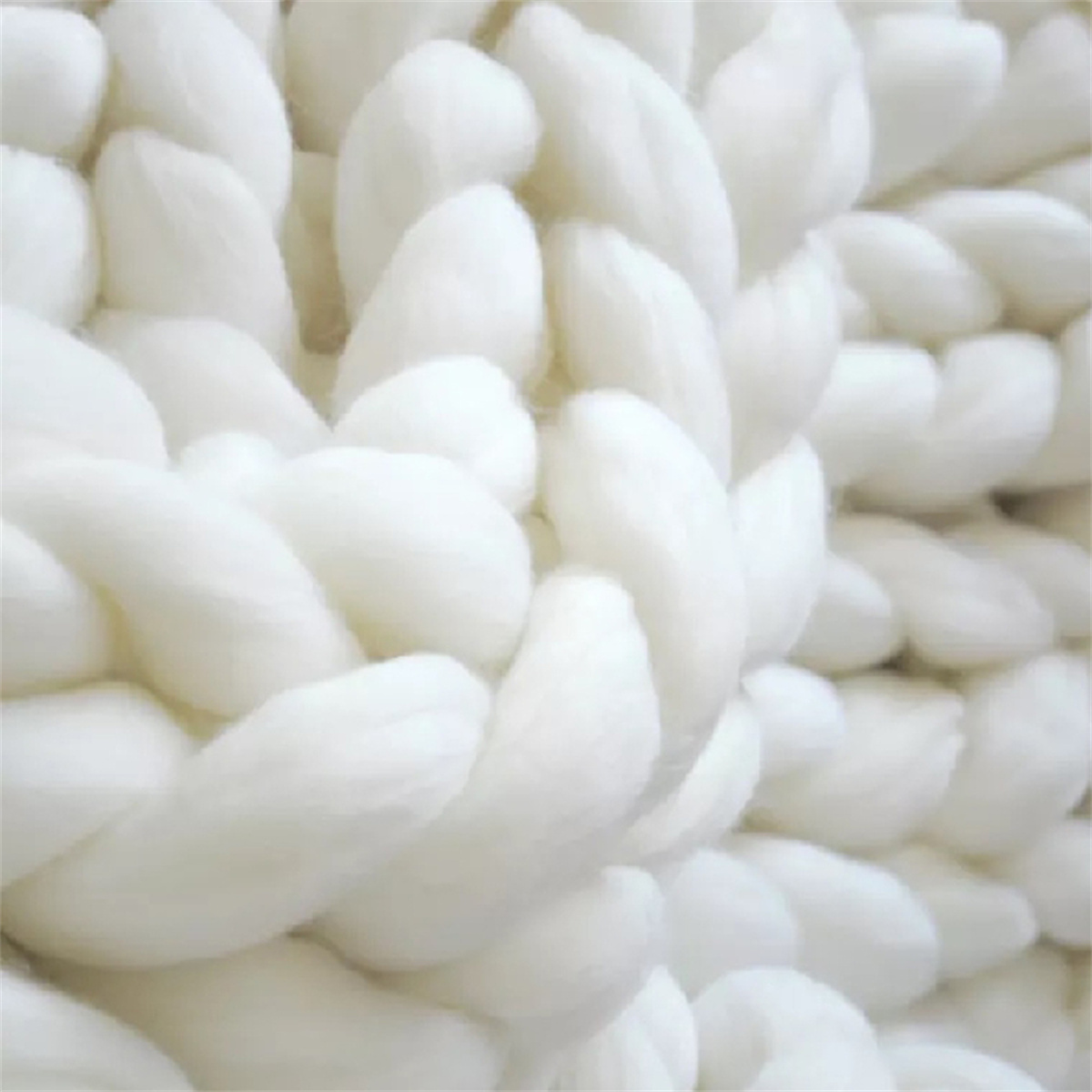 Nahaufnahme einer weißen, grob gestrickten Decke. Dicke, verwobene Stränge bilden eine strukturierte Oberfläche.