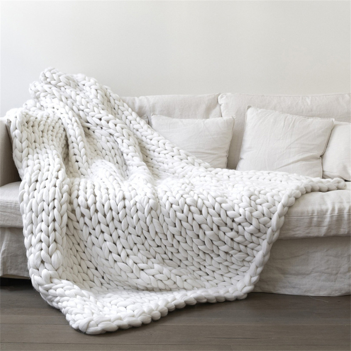 Weiße, grob gestrickte Decke auf einem weißen Sofa mit weißen Kissen und Holzboden.