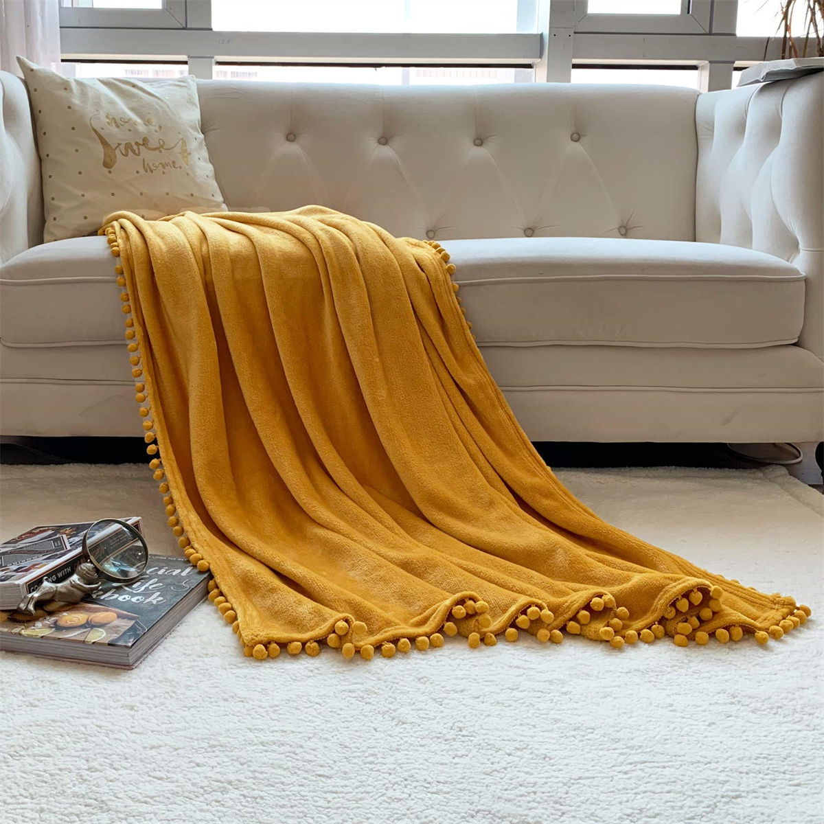 Gelbe Decke auf weißem Sofa, mit Kissen und Buch auf dem Boden.