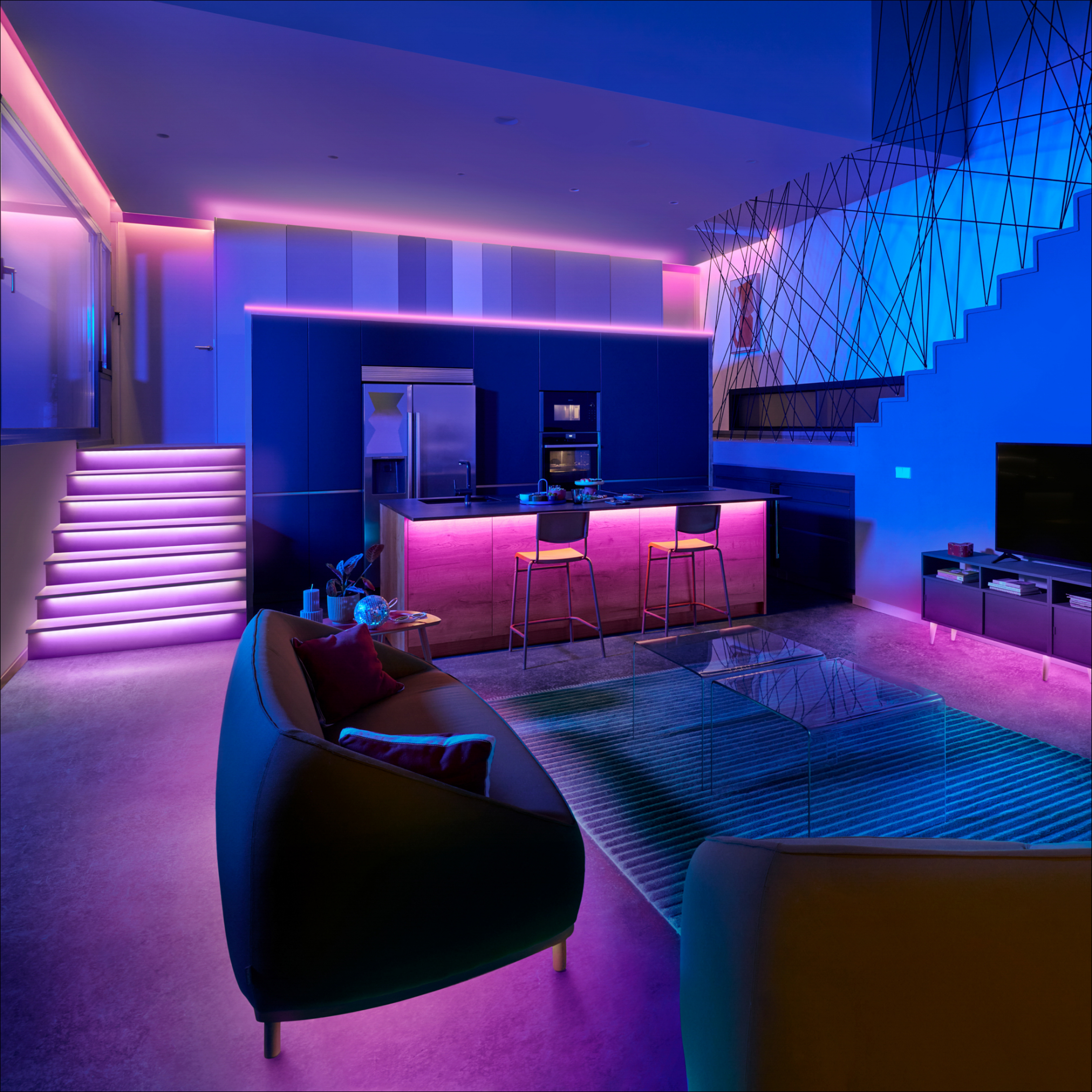 Modern room with blue and purple lighting. A black sofa, stairs, and kitchen island are visible.
