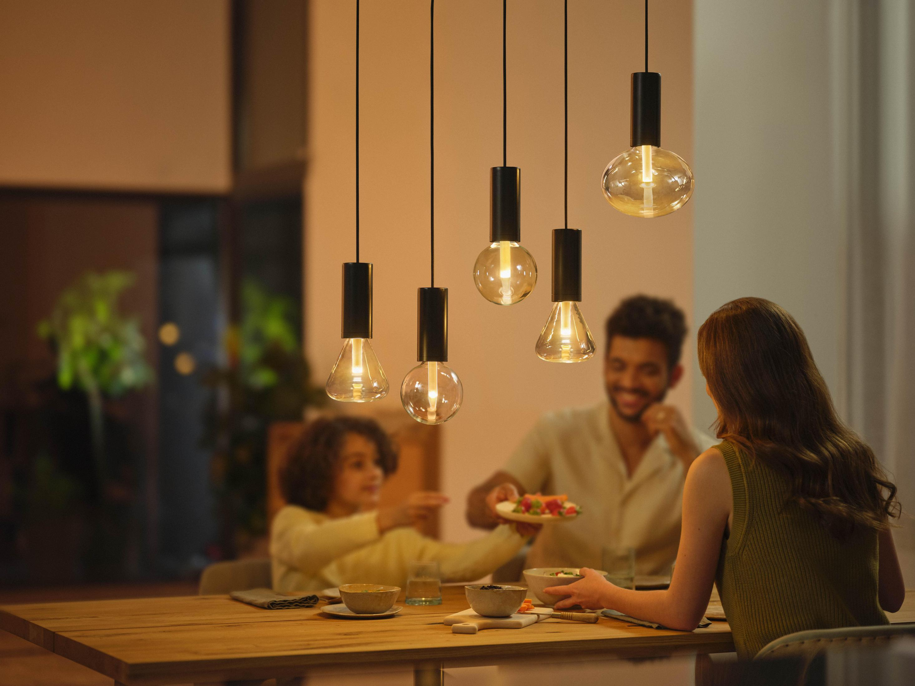 Una familia en una mesa de comedor, iluminada por luces colgantes, disfrutando de una comida juntos.