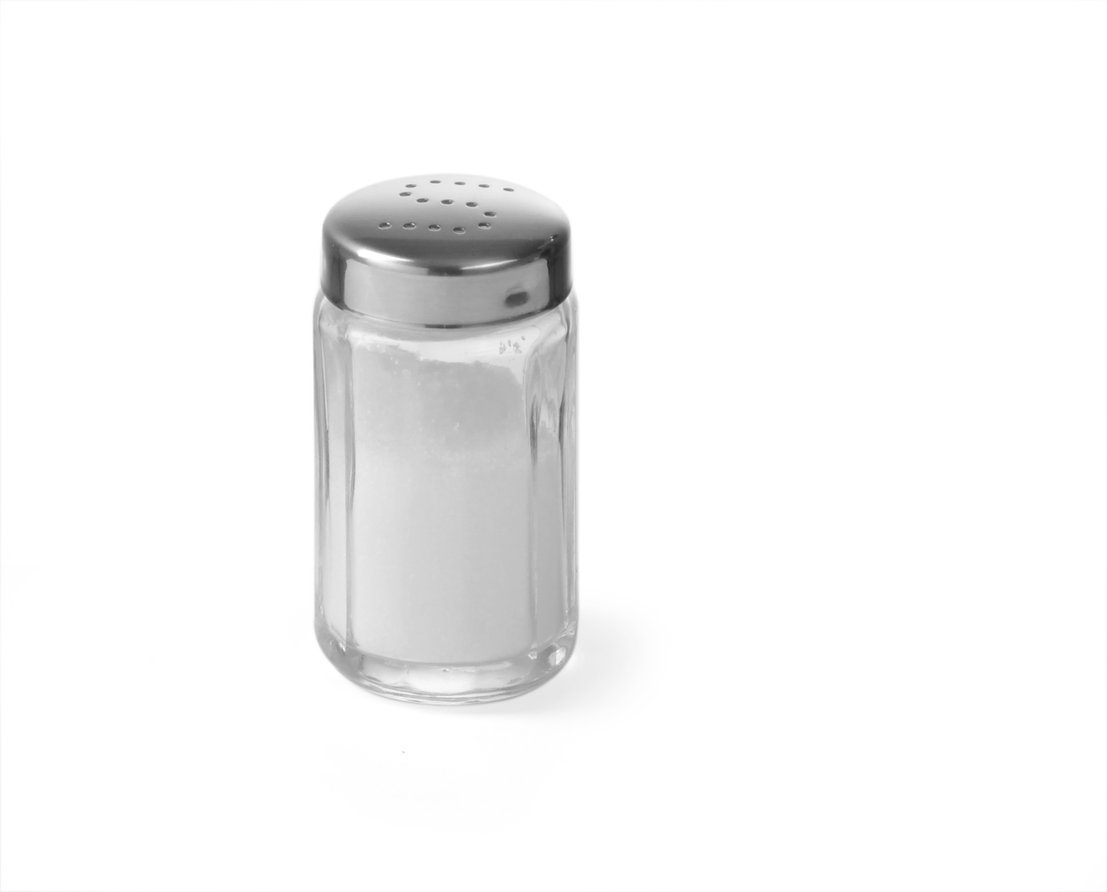 Un saliera di vetro trasparente con coperchio argentato, riempita di sale bianco.