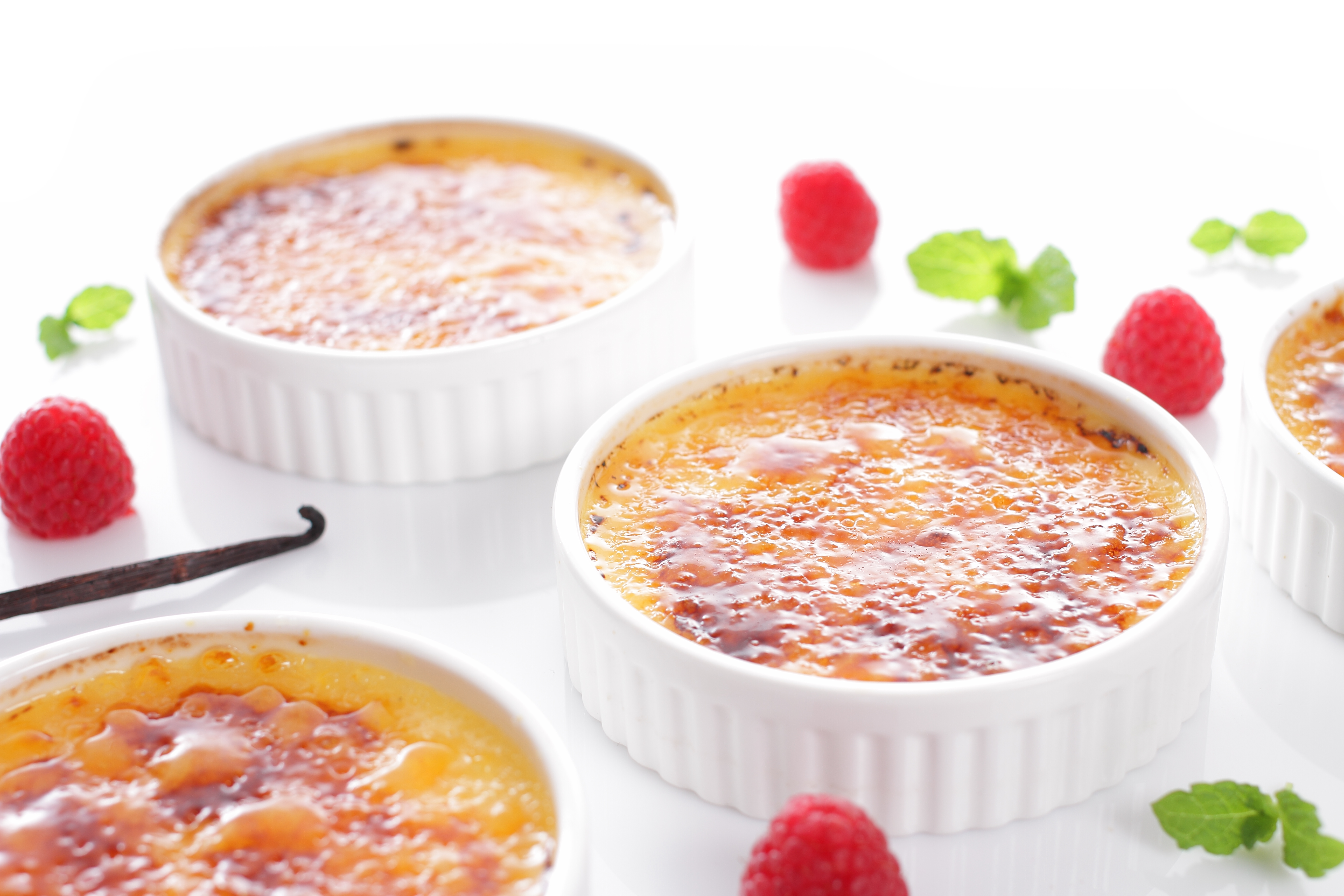 Crème brûlée in ramekin con lamponi, baccello di vaniglia e foglie di menta.