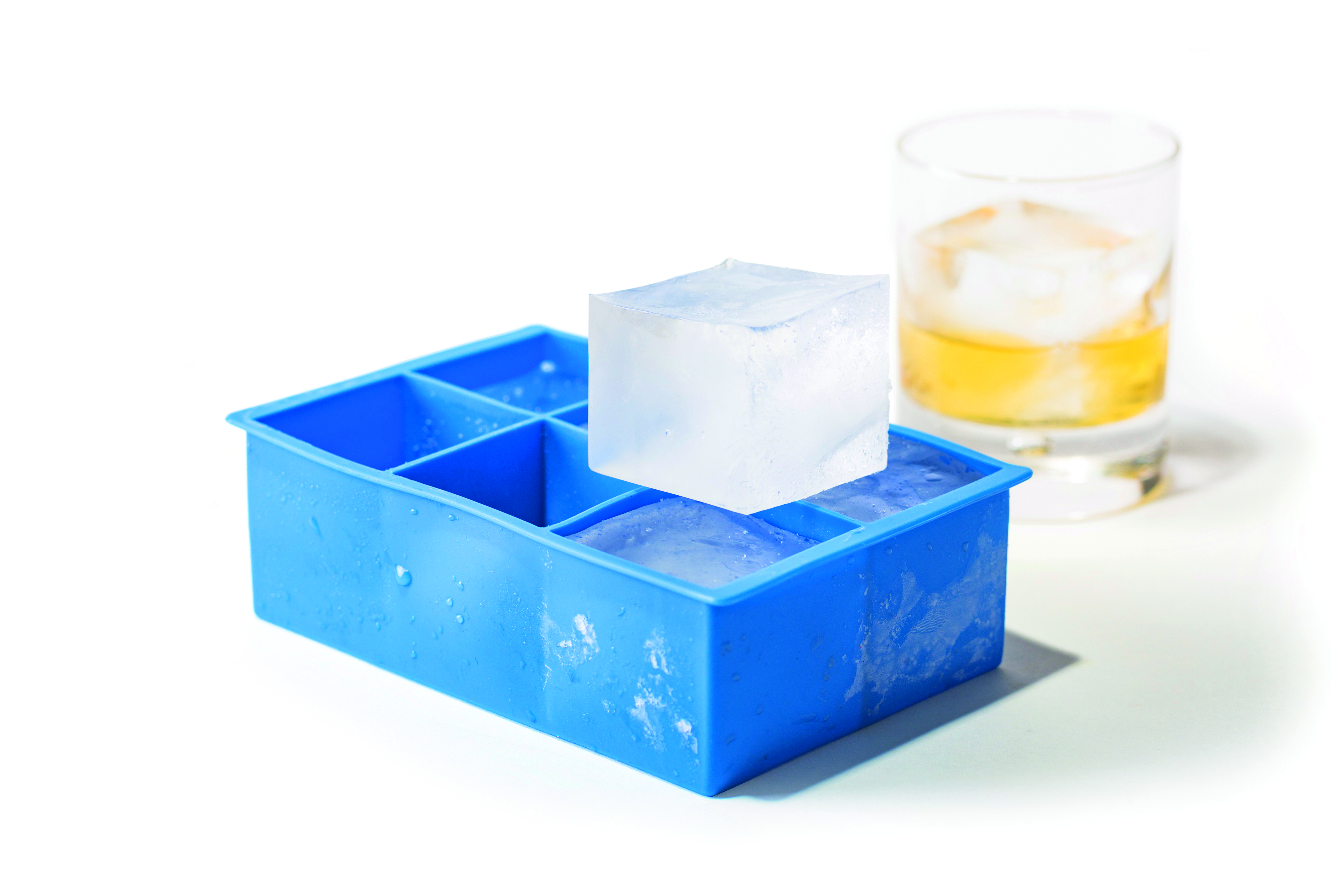 Vassoio blu per cubetti di ghiaccio, un cubo sopra, un bicchiere con bevanda.