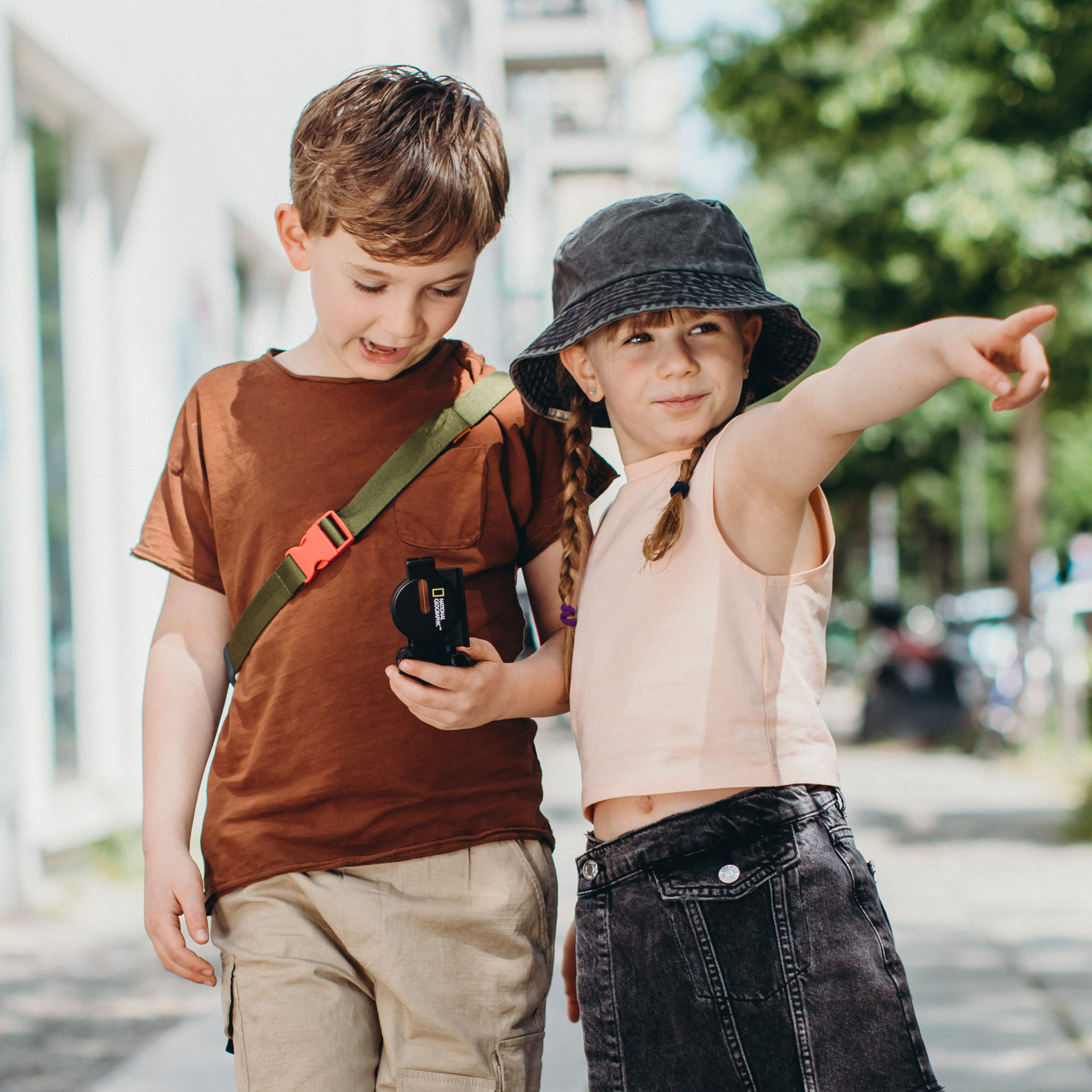 Un niño y una niña con sombrero sostienen una brújula y señalan hacia una dirección.
