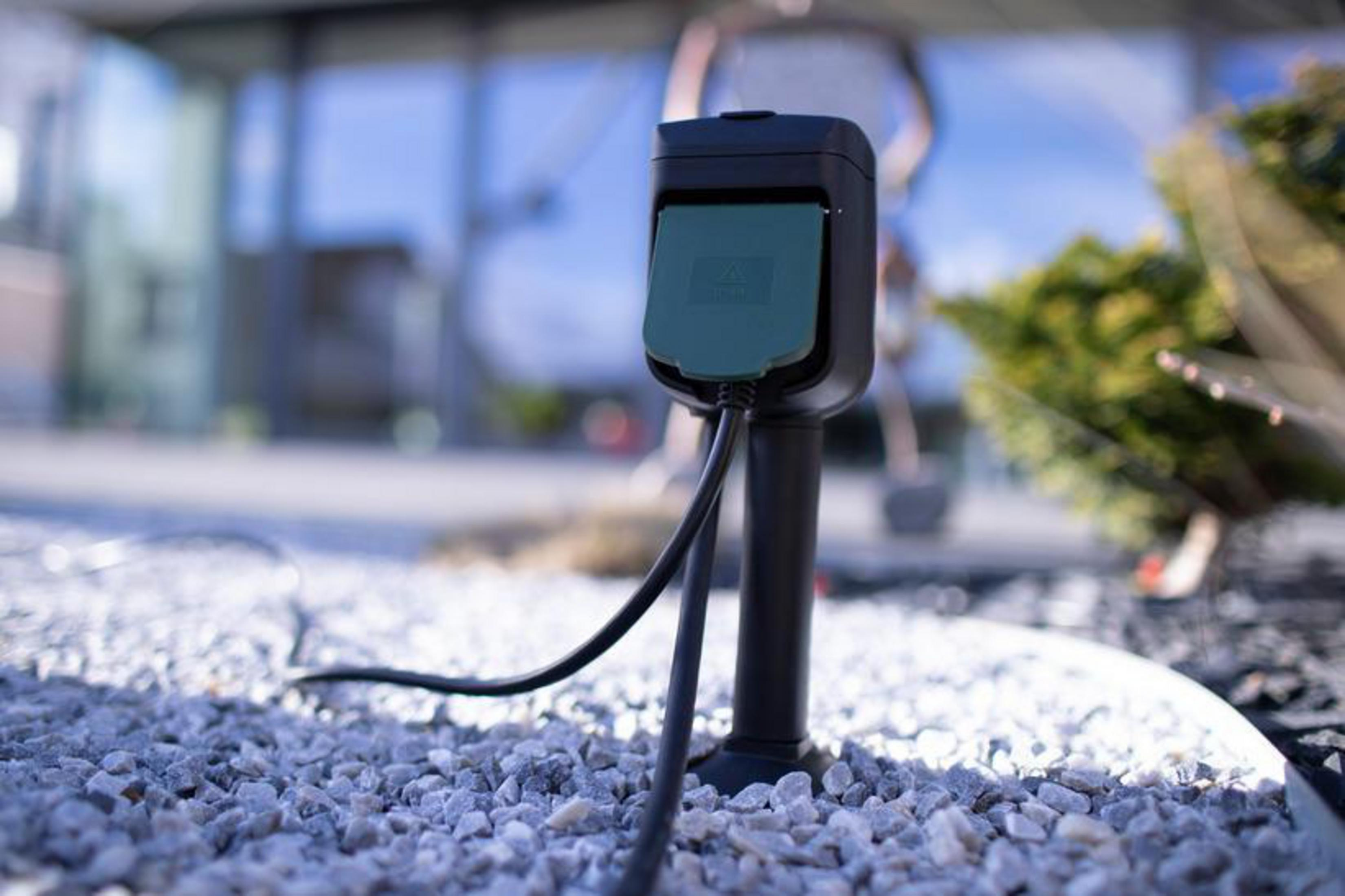 Presa di corrente esterna. Nera e verde, montata su un palo nero in un giardino con ciottoli.
