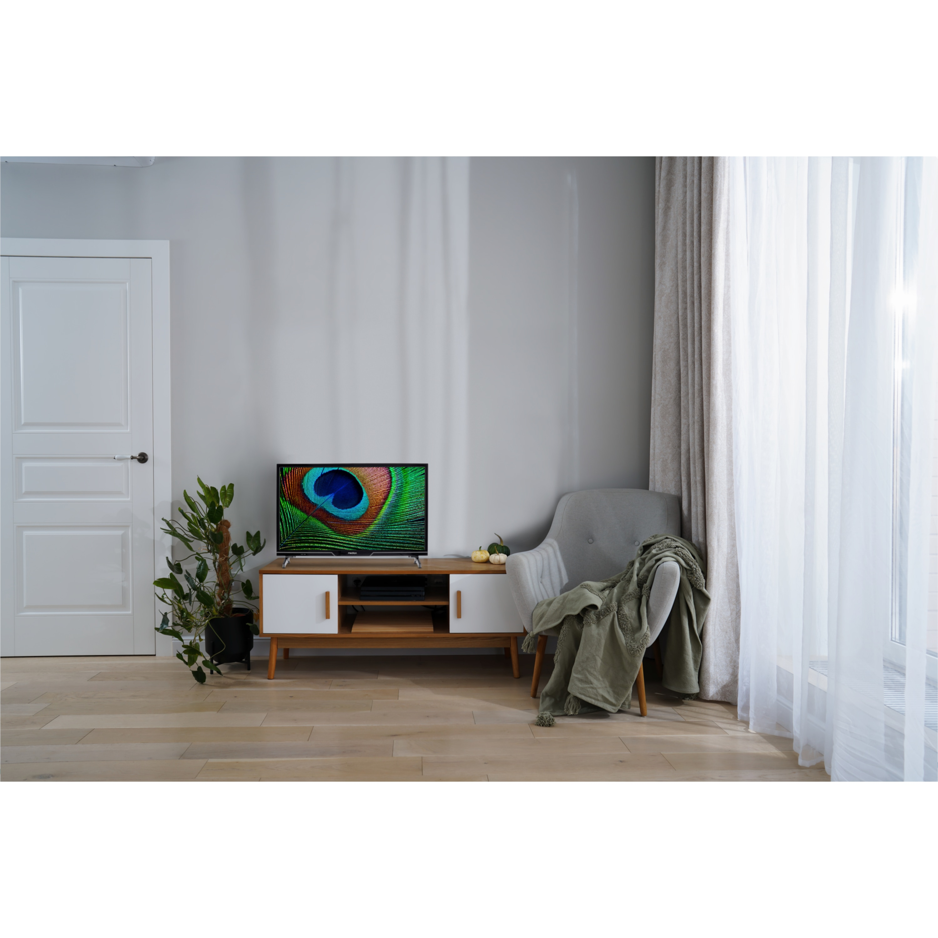 Een woonkamer met een tv op een wit en bruin tv-meubel. Een bank, gordijnen en een kamerplant zijn ook zichtbaar.