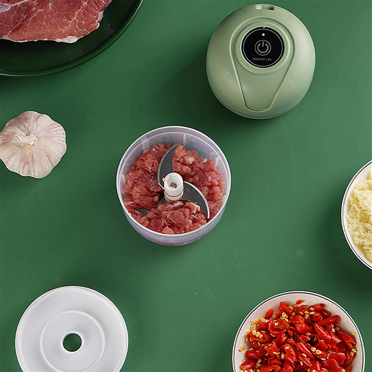 Zerkleinerer mit gehacktem Fleisch, Knoblauch und Chilischoten auf grüner Fläche.