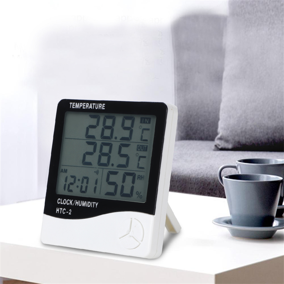 Digitale Uhr/Feuchtigkeitsmesser. Text: Temperatur, Uhr/Feuchtigkeit. Zwei Tassen im Hintergrund.