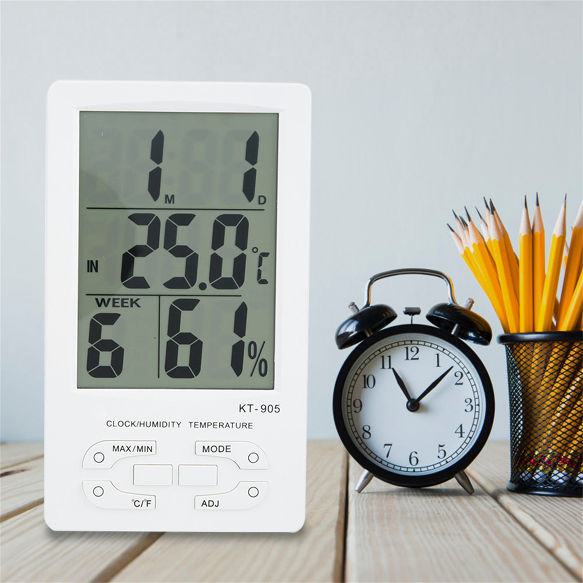 Weiße Digitaluhr, schwarzer Wecker und Bleistifte. Uhr zeigt Zeit und Temperatur.