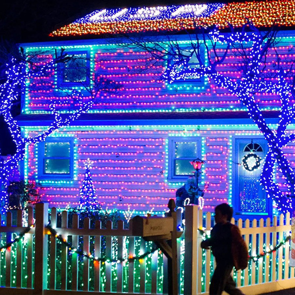 Haus mit bunten Weihnachtsbeleuchtungen. Ein Kind rennt an einem Zaun im Vordergrund vorbei.