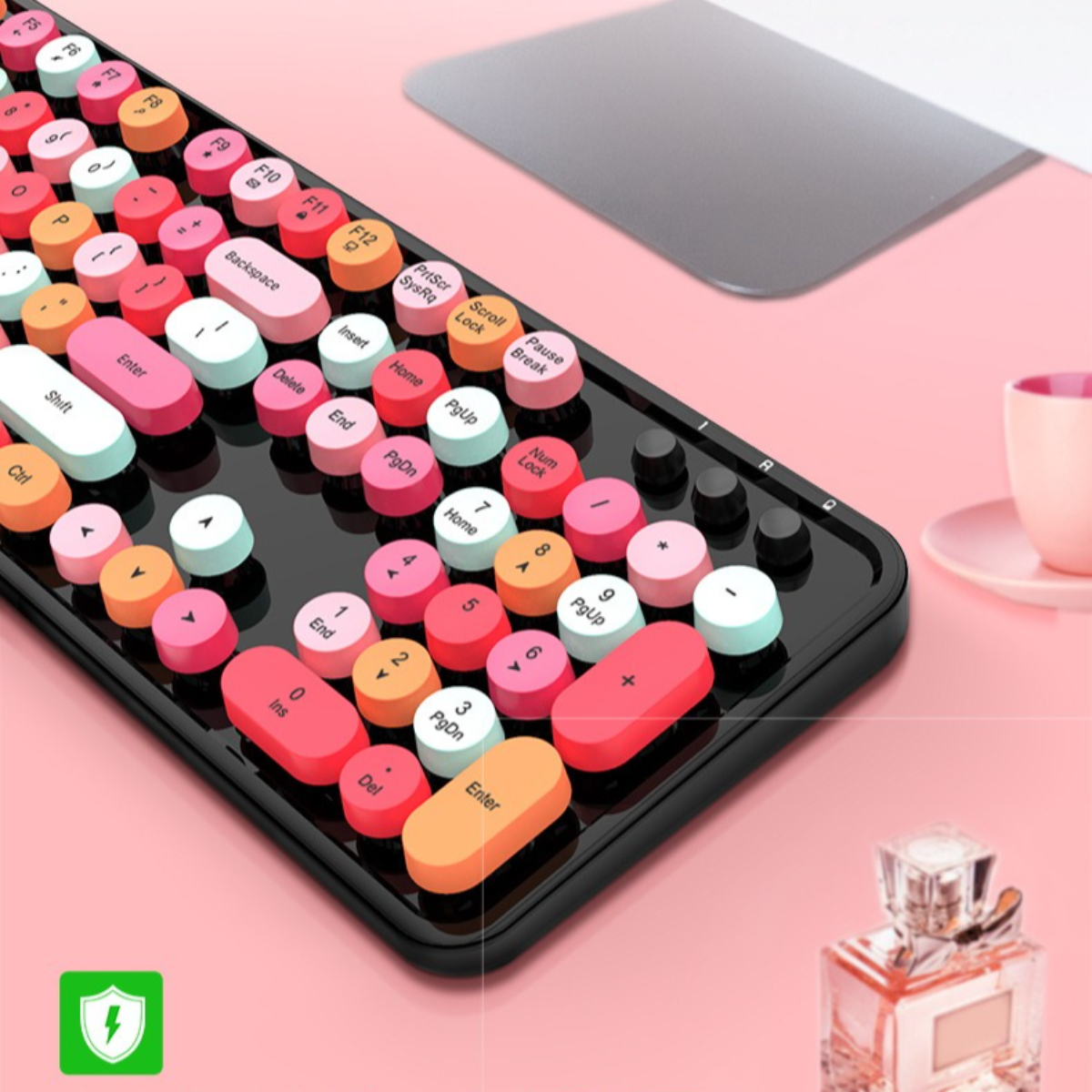 Bunte runde Tastatur mit pinkem Hintergrund. Eine Tasse und Parfüm sind daneben.