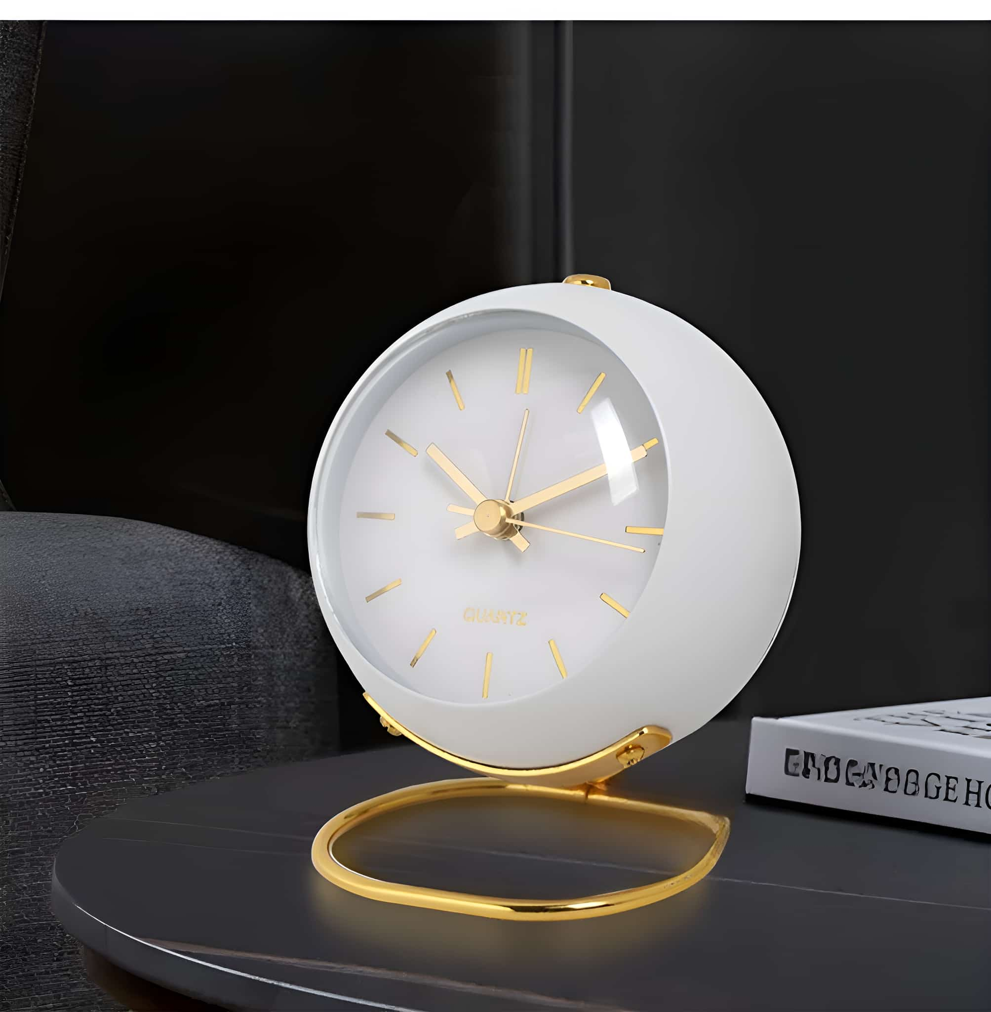 Eine weiße, runde Uhr mit goldenen Details und einem goldenen Ständer. Die Uhr steht auf einem dunklen Tisch.
