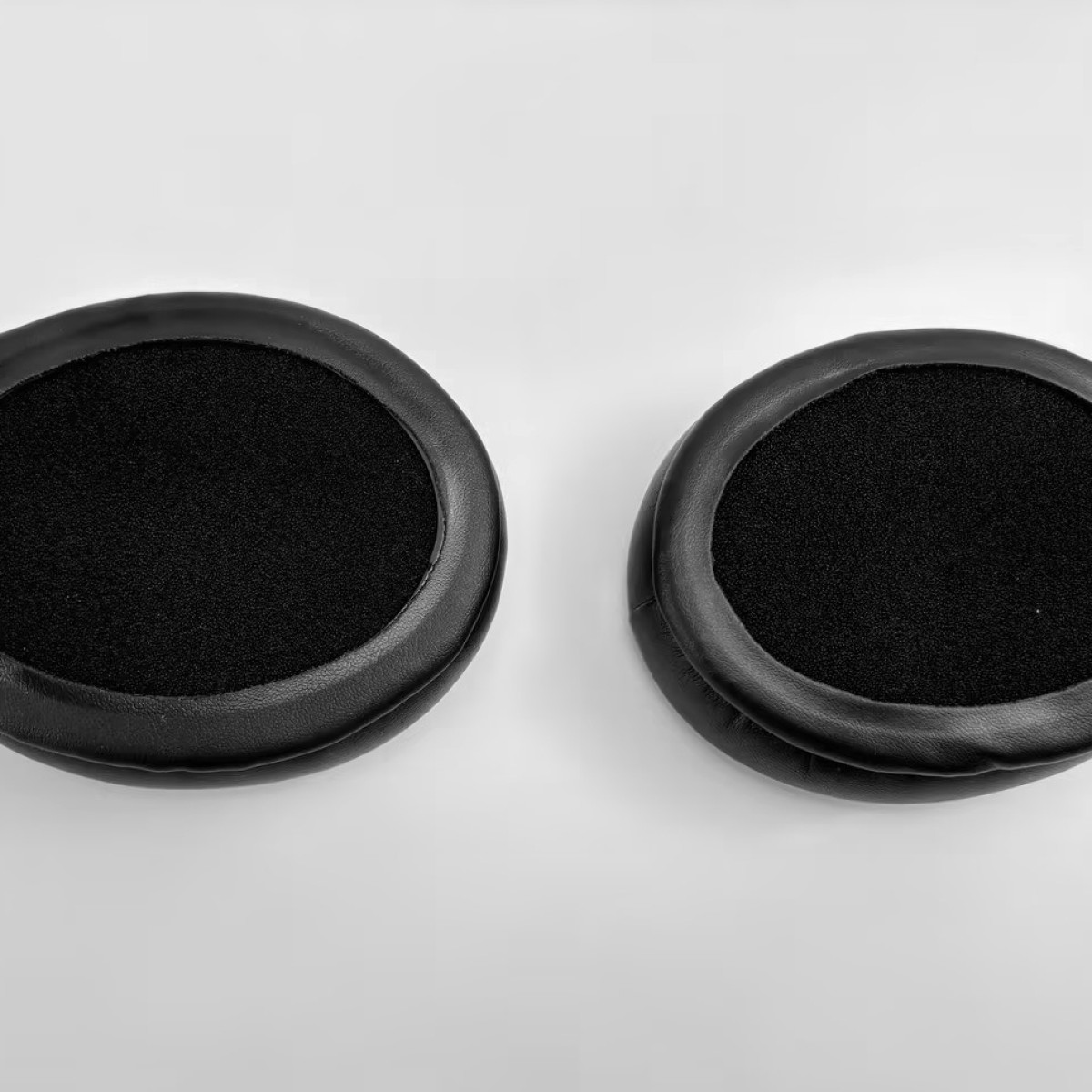 Dwie czarne poduszki nauszne do słuchawek na białym tle. Czarne poduszki są okrągłe.