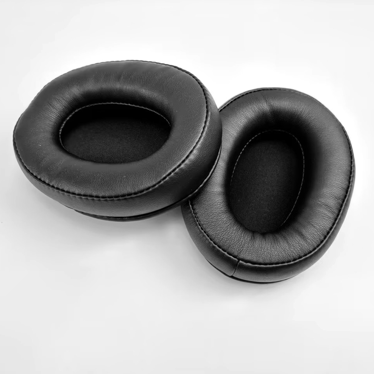Dwie czarne, owalne poduszki na uszy słuchawek na białej powierzchni.