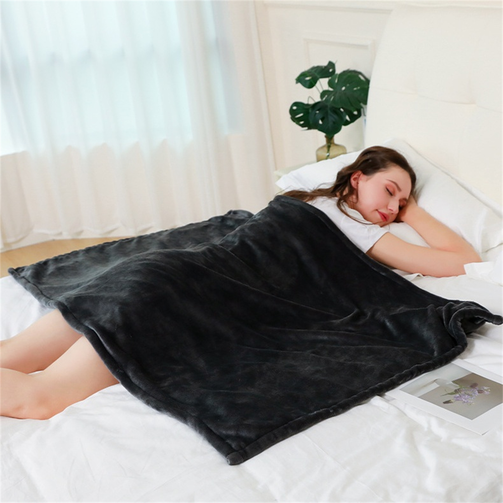 Frau schläft unter einer dunkelgrauen Decke auf einem Bett mit weißen Laken.