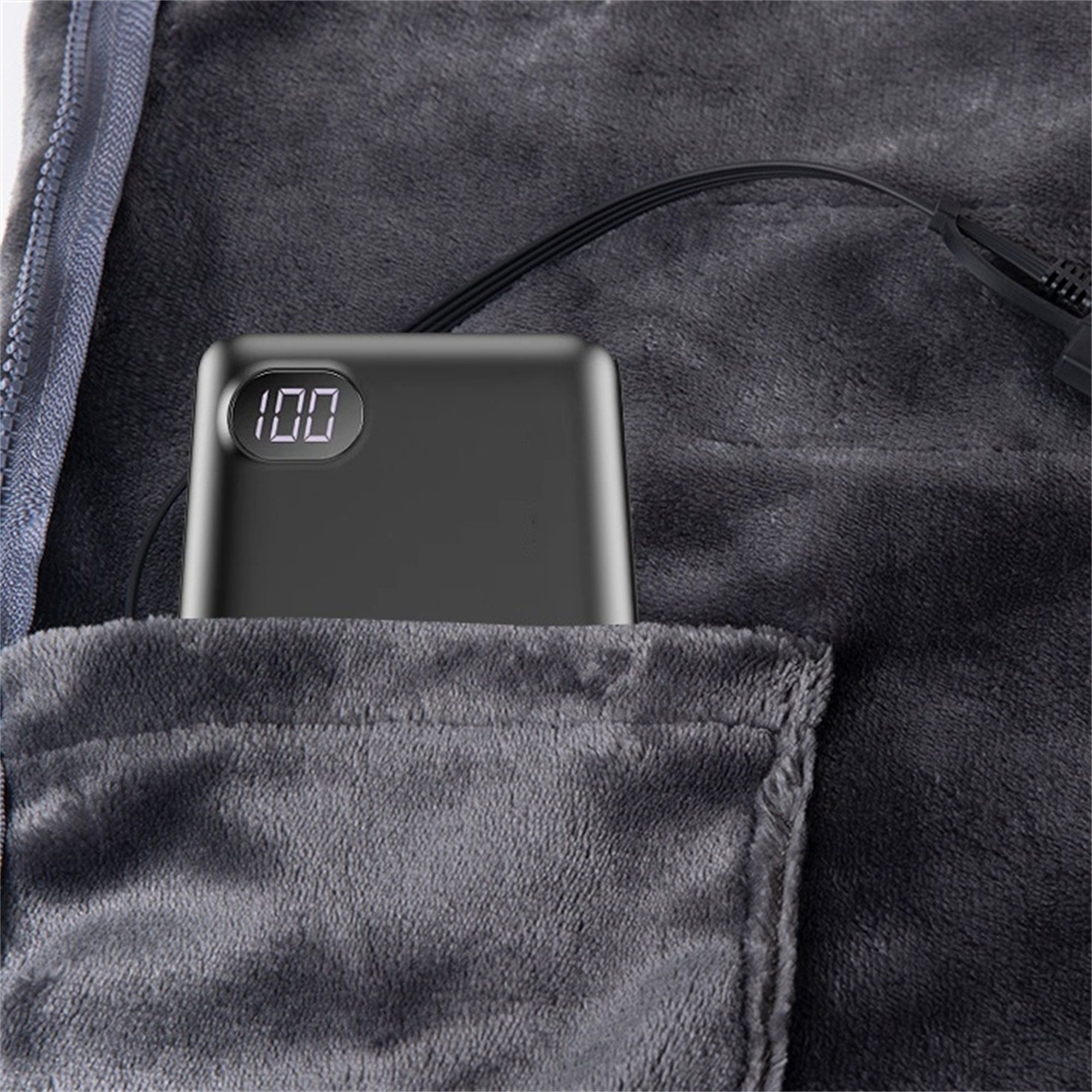 Schwarze Powerbank in einer Tasche einer grauen Decke mit digitaler Anzeige.
