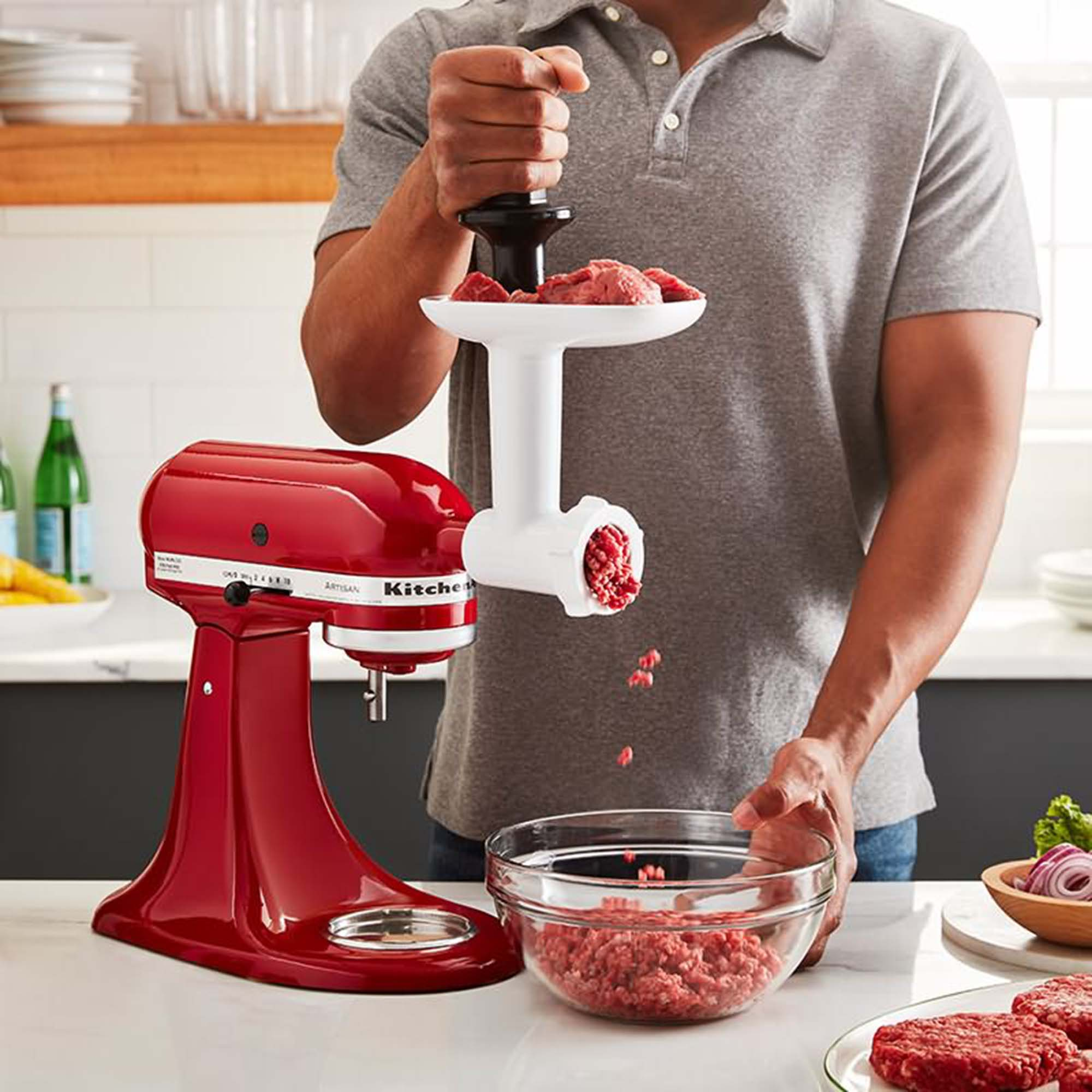 Osoba używa miksera KitchenAid z przystawką do mielenia mięsa, mieląc mięso do miski.