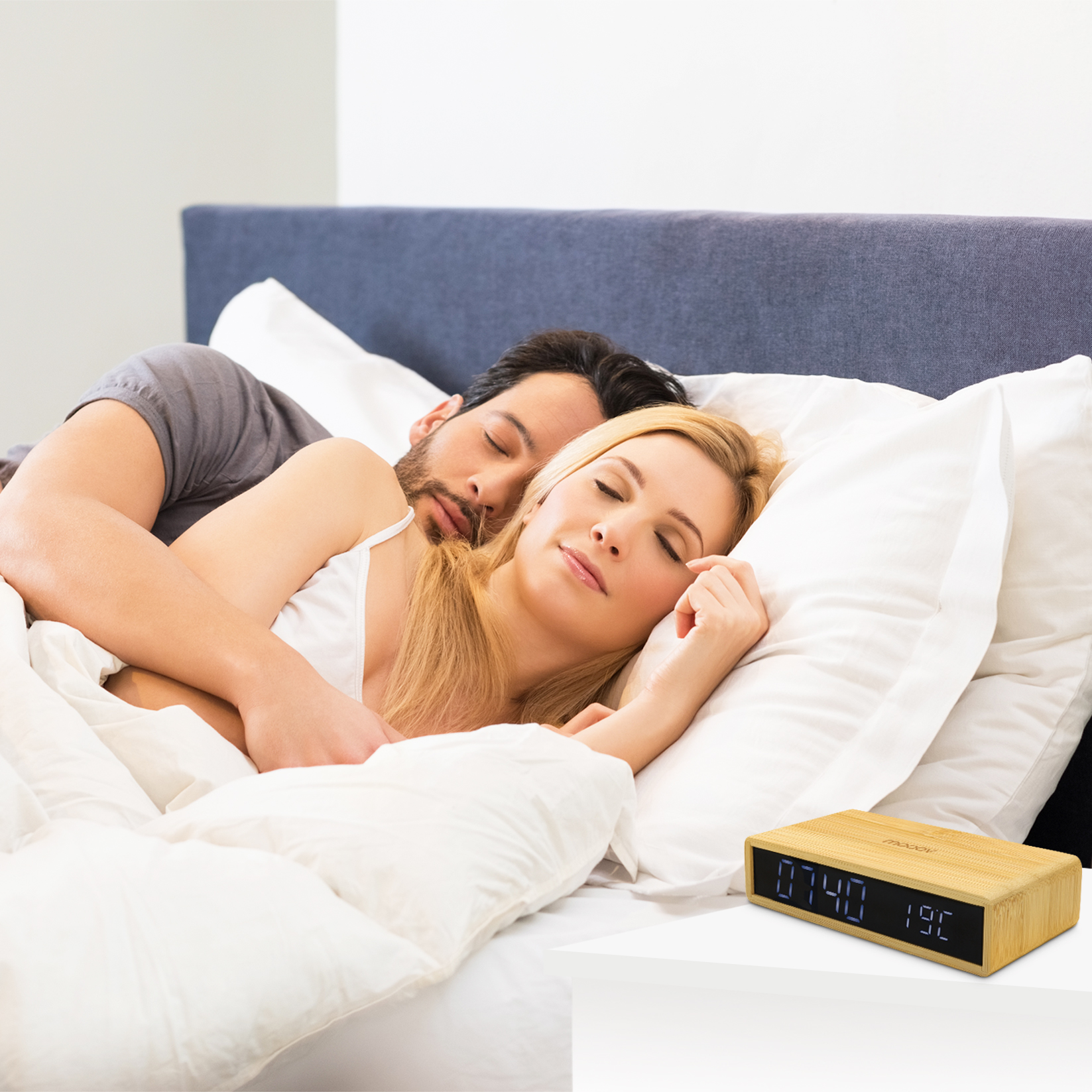 Una pareja durmiendo en la cama. Un reloj de madera con pantalla digital está en la mesita de noche.