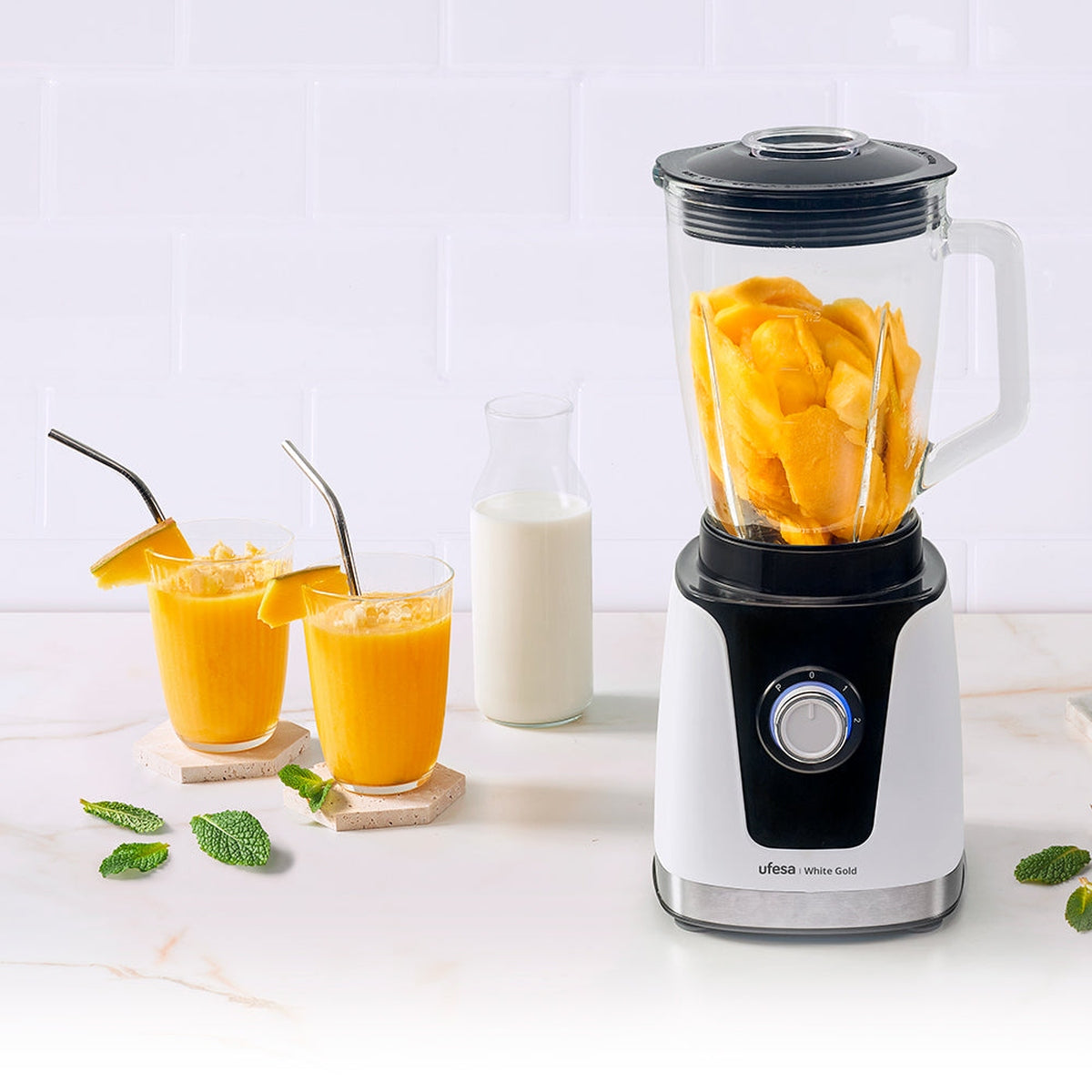 Frullatore con mango, latte e due bicchieri di succo di mango.