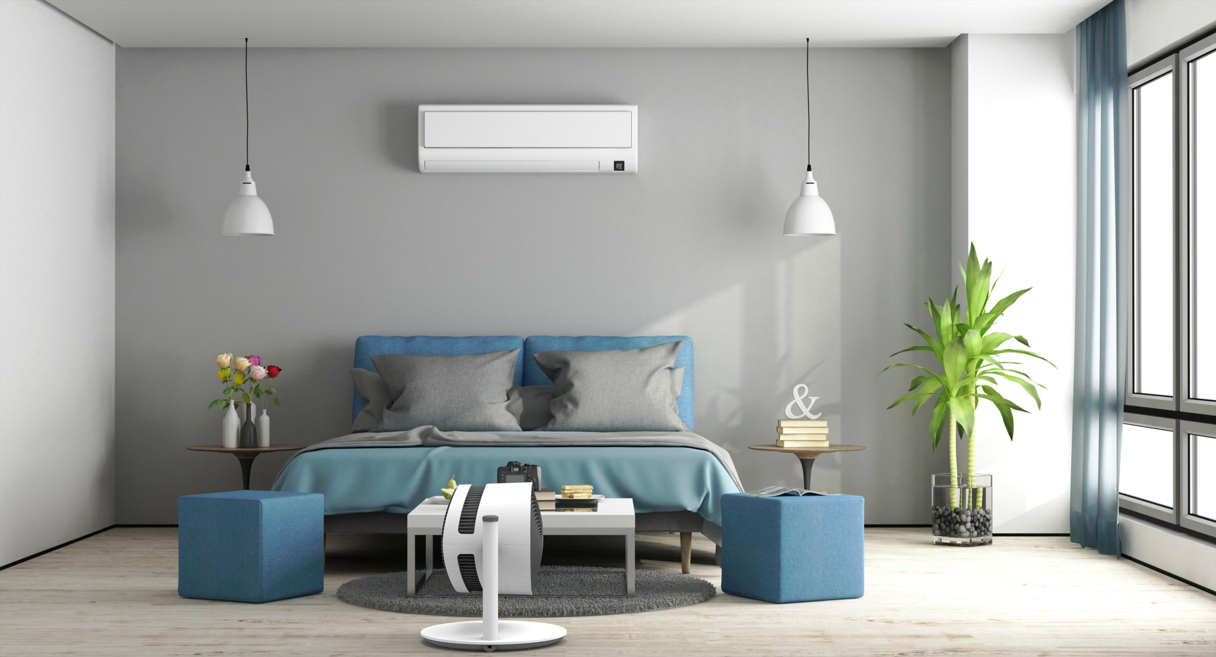 Schlafzimmer mit Bett, Beistelltischen und Klimaanlage. Blaue Akzente, zwei Pendelleuchten und ein großes Fenster.