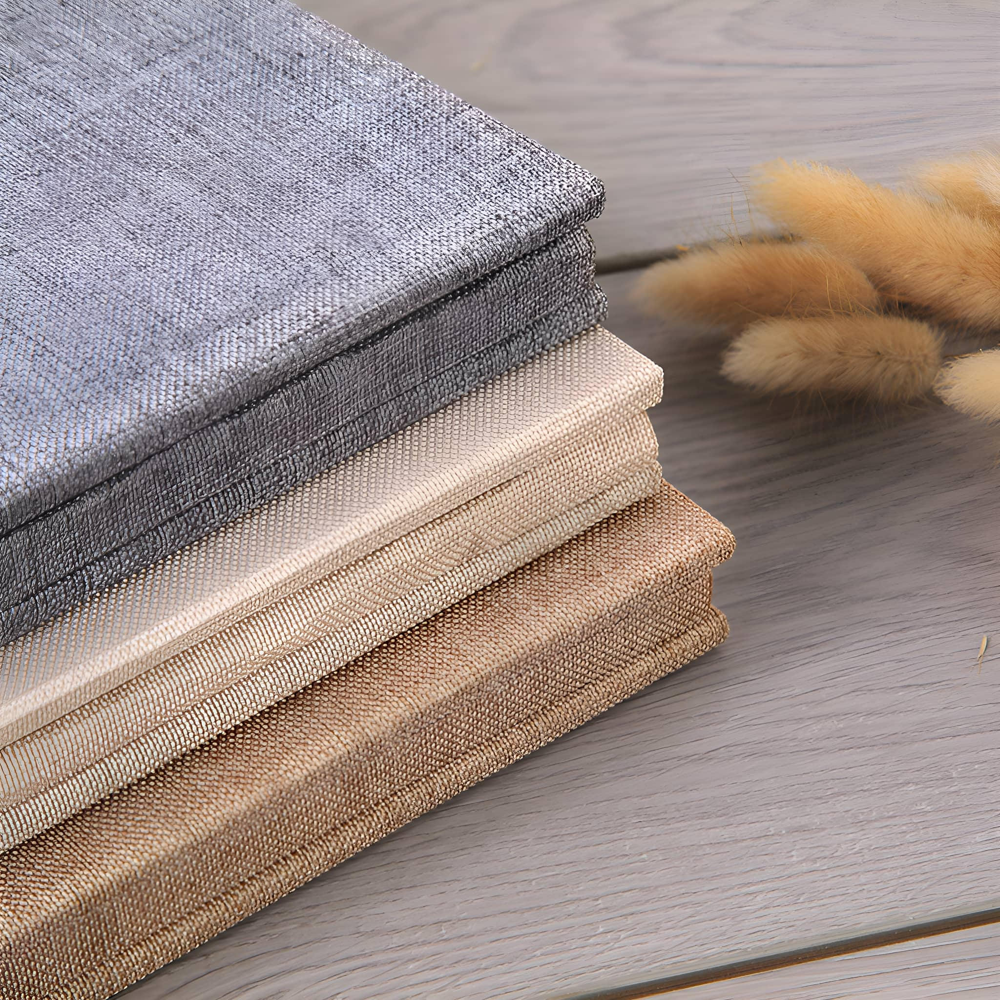 Stapel von vier Stoffmustern in gedeckten Tönen: Grau, Anthrazit, Off-White und Beige.