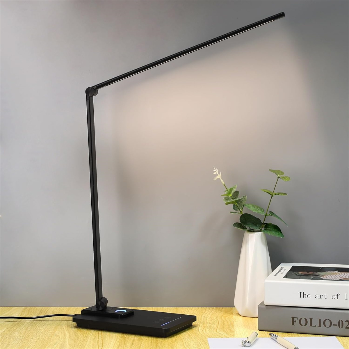 Schwarze Schreibtischlampe mit langem Hals, Ladebasis und Vase mit Pflanze.