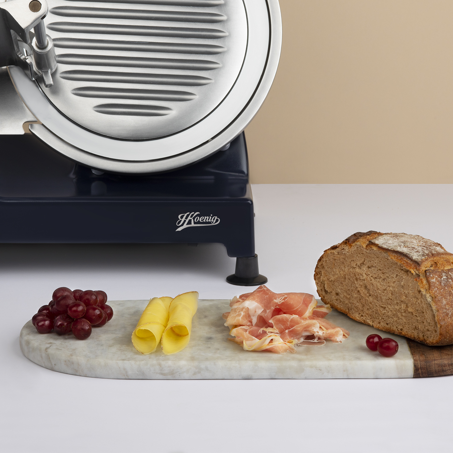 Krajalnica do żywności z chlebem, winogronami, serem i szynką na marmurowej desce.