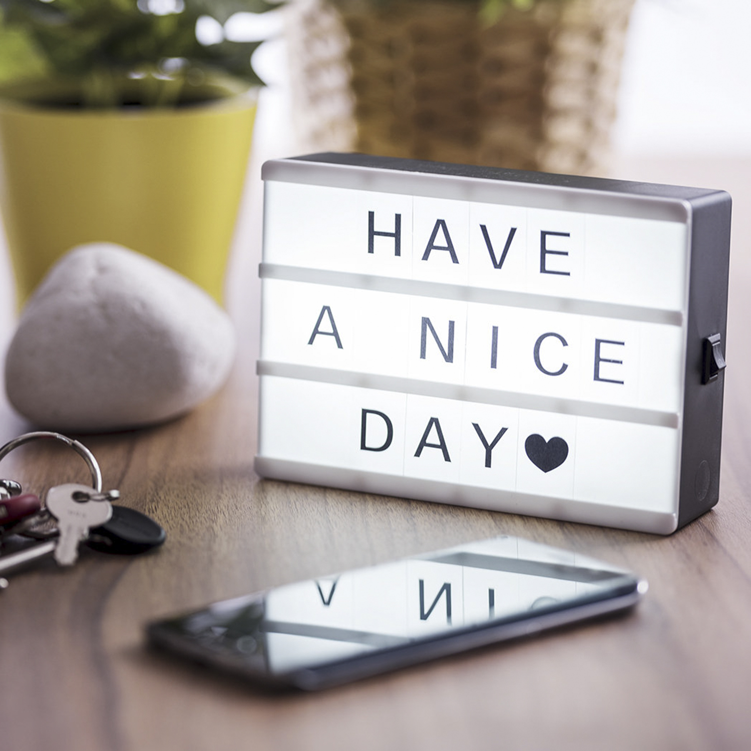Un letrero iluminado que dice "HAVE A NICE DAY" con un corazón, junto a un teléfono y llaves.