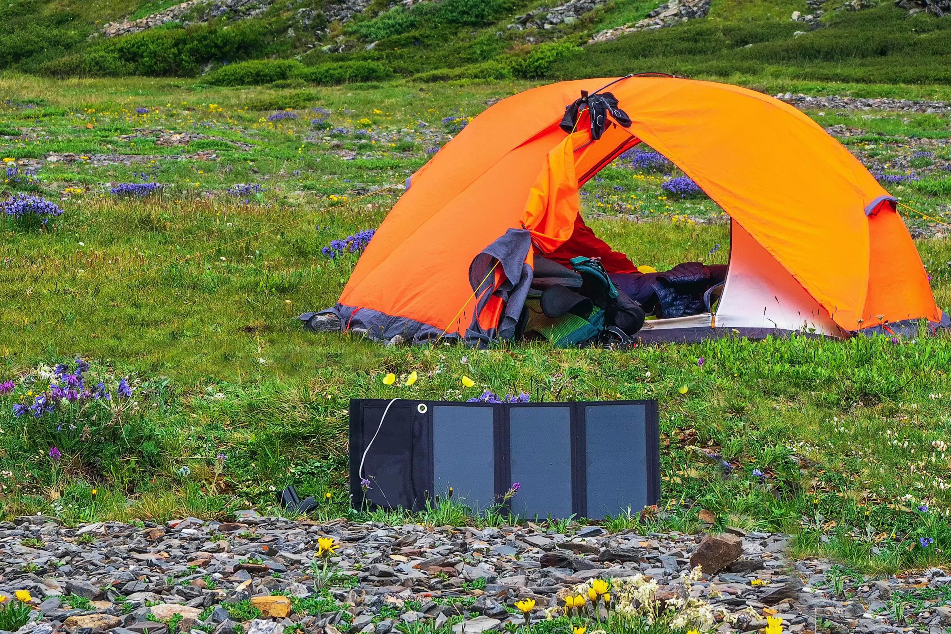 Pomarańczowy namiot rozbity na trawiastym polu, z panelem słonecznym na pierwszym planie.
