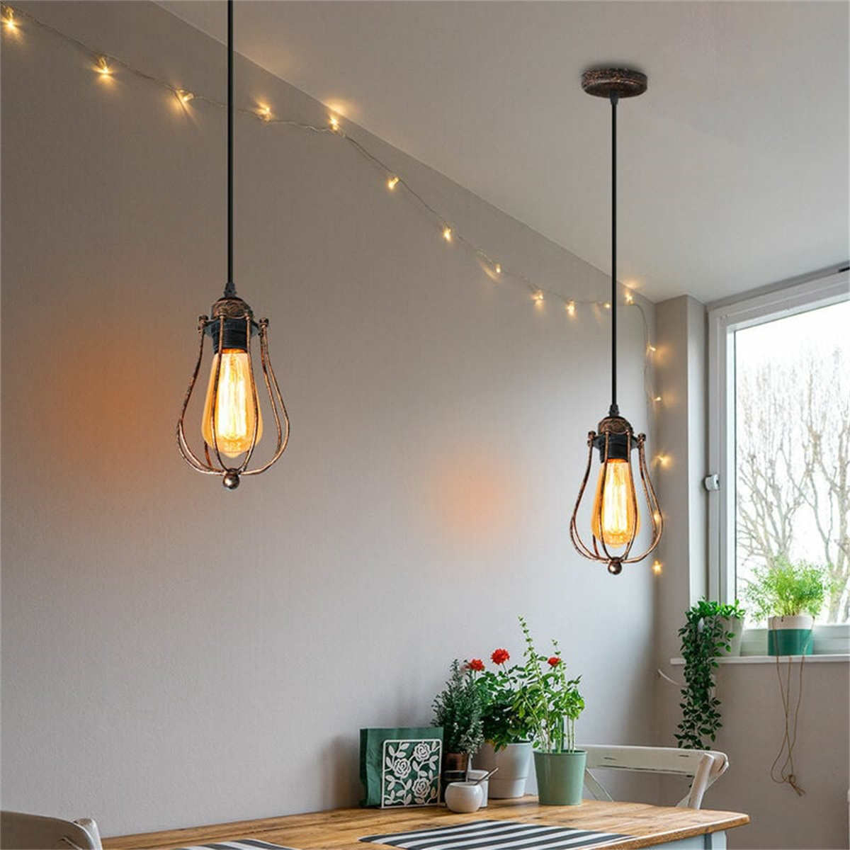 Zwei hängende Pendelleuchten mit Edison-Glühbirnen über einem Holztisch mit Blumen und Lichterketten.