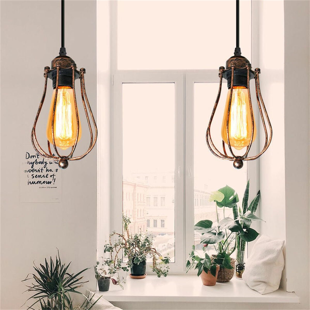 Zwei Hängelampen mit freiliegenden Glühbirnen und ein Fenster mit Pflanzen werden gezeigt. Die Lampen sind golden.