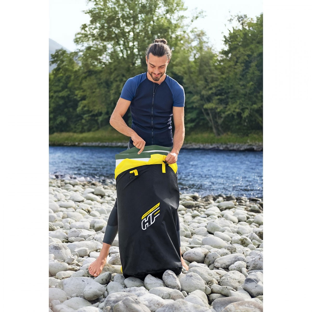 Mężczyzna otwiera czarno-żółtą torbę. Jest na skalistym brzegu, w tle rzeka.