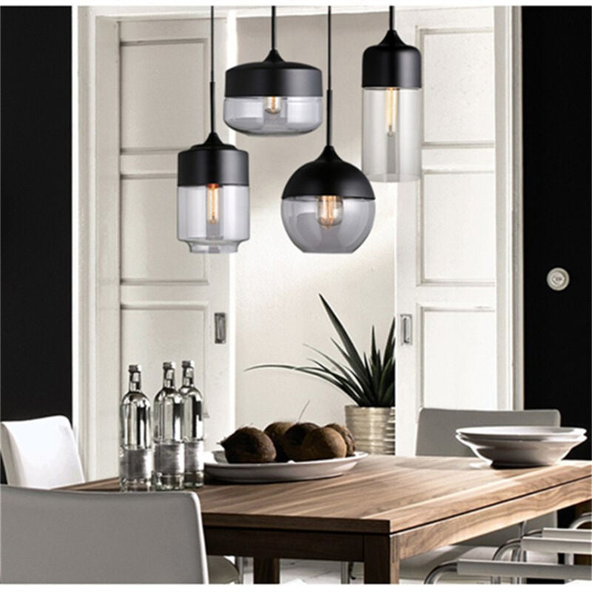 Drei hängende Pendelleuchten mit schwarzen Oberteilen und Glasschirmen über einem Holztisch.