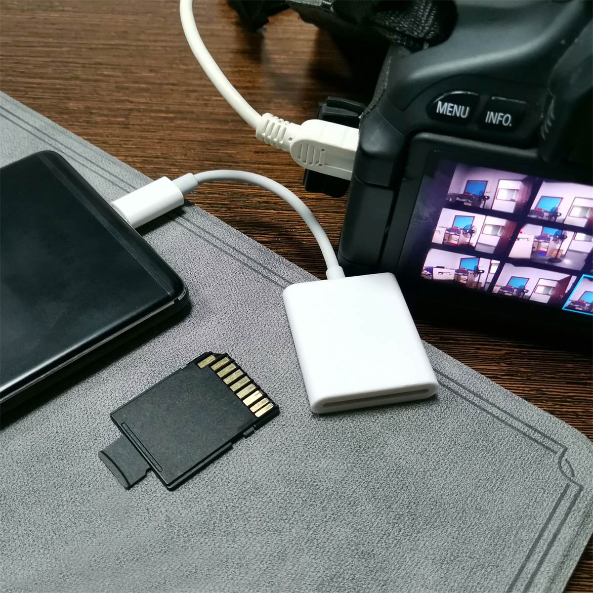 Ein Smartphone, eine SD-Karte und ein weißer Adapter, der über ein USB-Kabel mit einer Kamera verbunden ist. Holztisch, graue Matte.