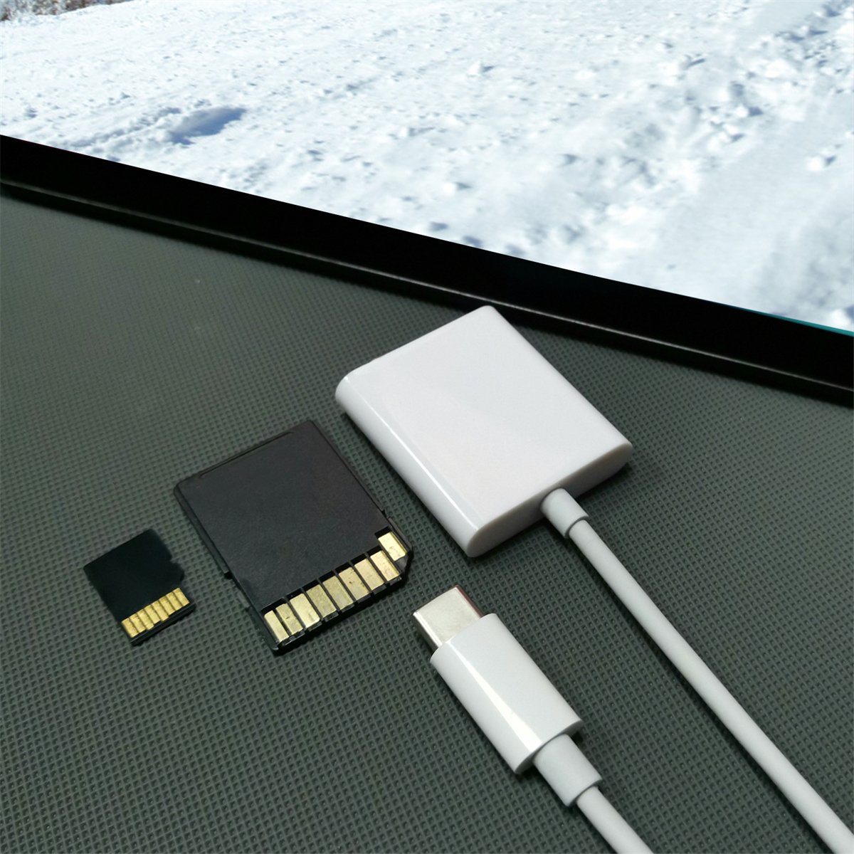 Verschiedene Datenspeichergeräte und Adapter auf dunkler Oberfläche mit verschneitem Hintergrund und weißem Adapter.