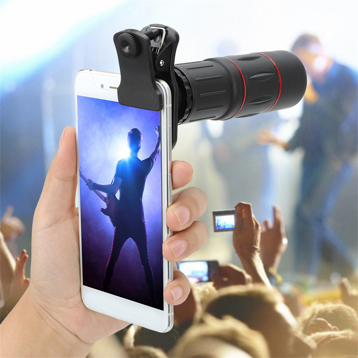 Hand hält Telefon mit Objektiv, zeigt Person, die Gitarre spielt. Publikum im Hintergrund.