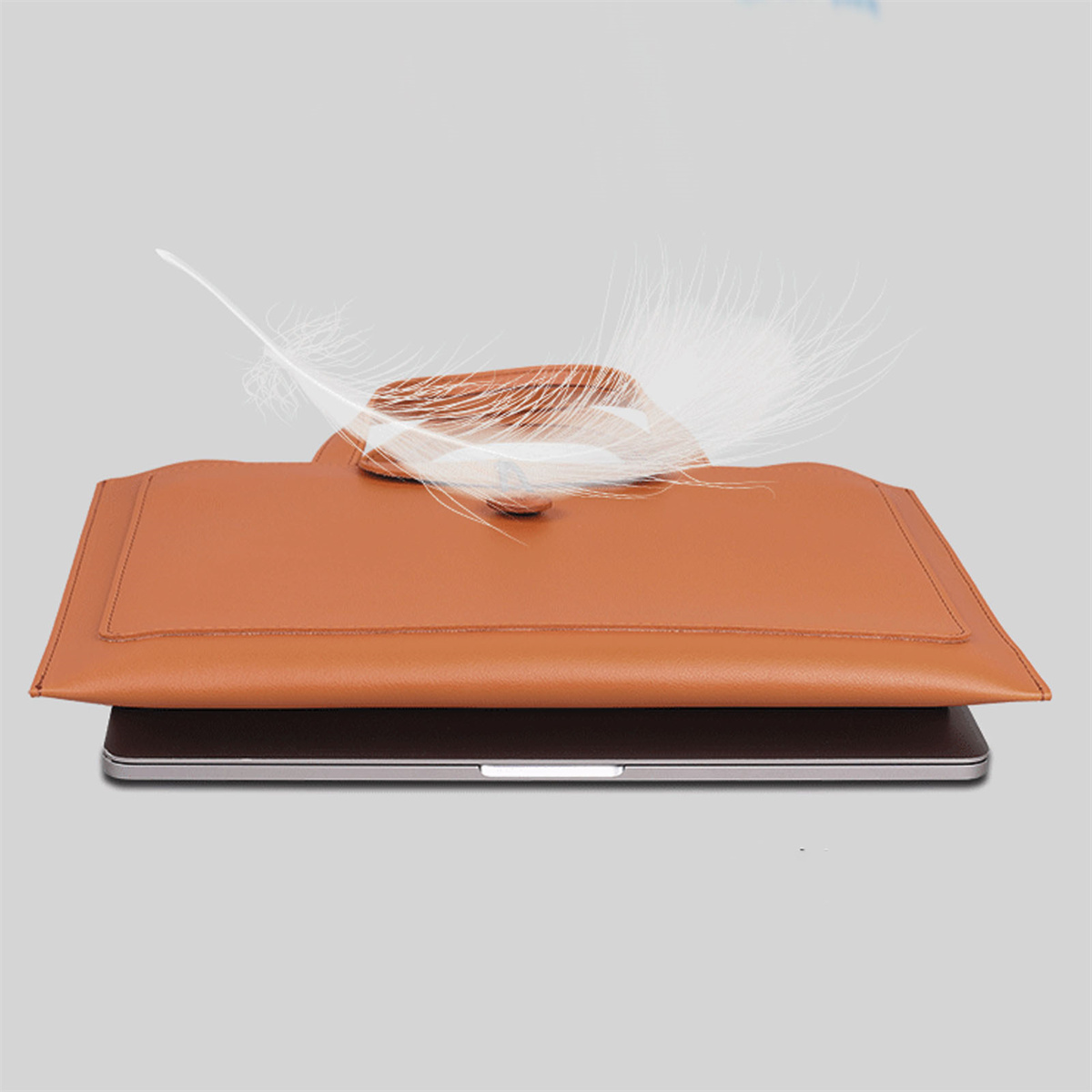 Braune Laptoptasche aus Leder mit Feder oben drauf. Der Laptop ist darin.