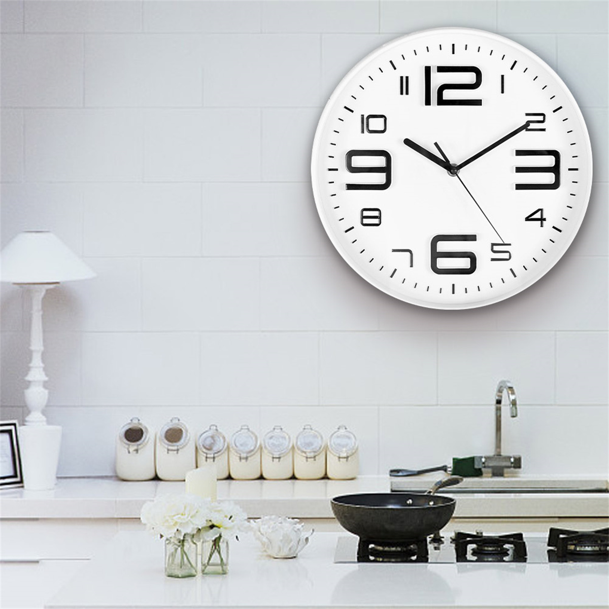 Weiße Küche mit weißer Wanduhr, die 10:10 anzeigt. Ein Herd, Pfannen und Blumen sind im Vordergrund.