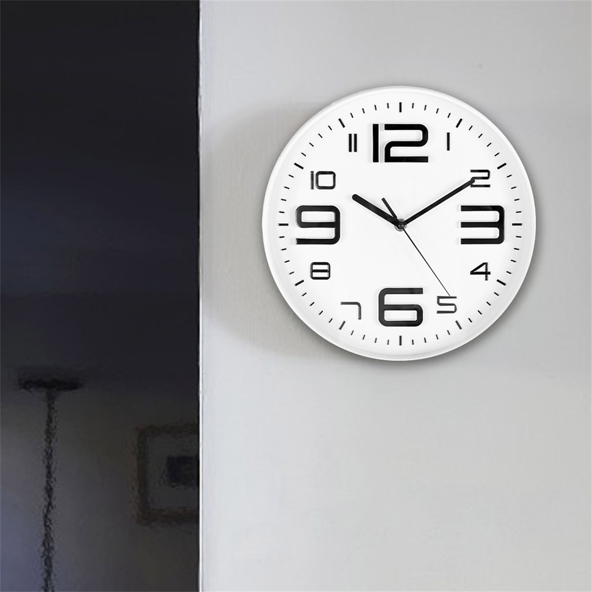 Eine weiße Uhr mit schwarzen Zahlen und Zeigern, montiert an einer hellgrauen Wand.