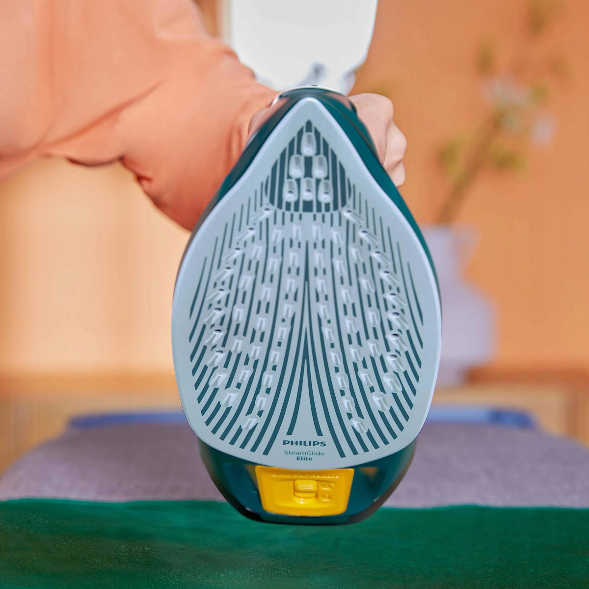 Zbliżenie podstawy żelazka Philips, zielone, z żółtym guzikiem. Ręka trzyma żelazko.