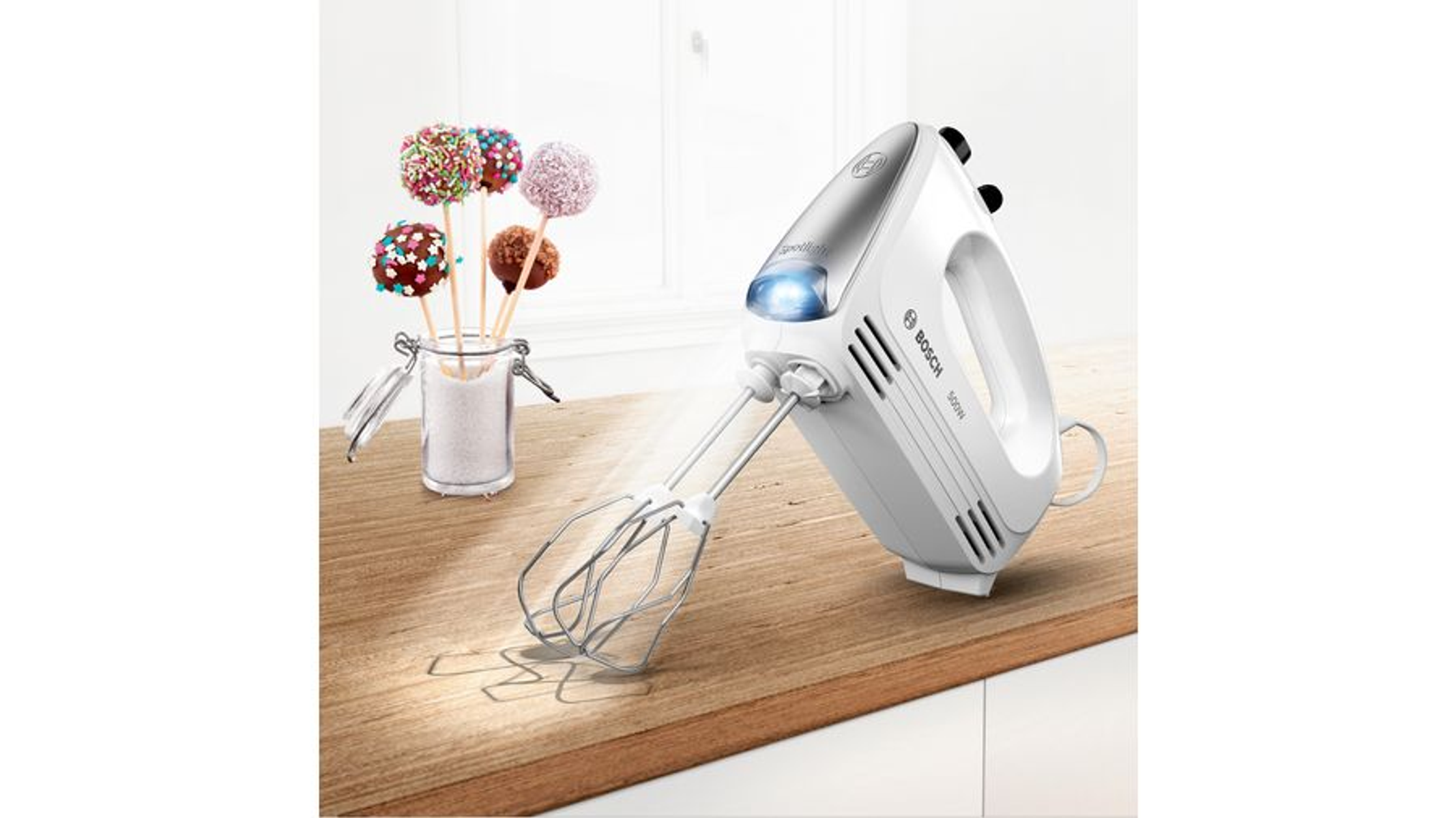 Weißer Bosch Handmixer auf Holz. Cake Pops im Glas im Hintergrund.