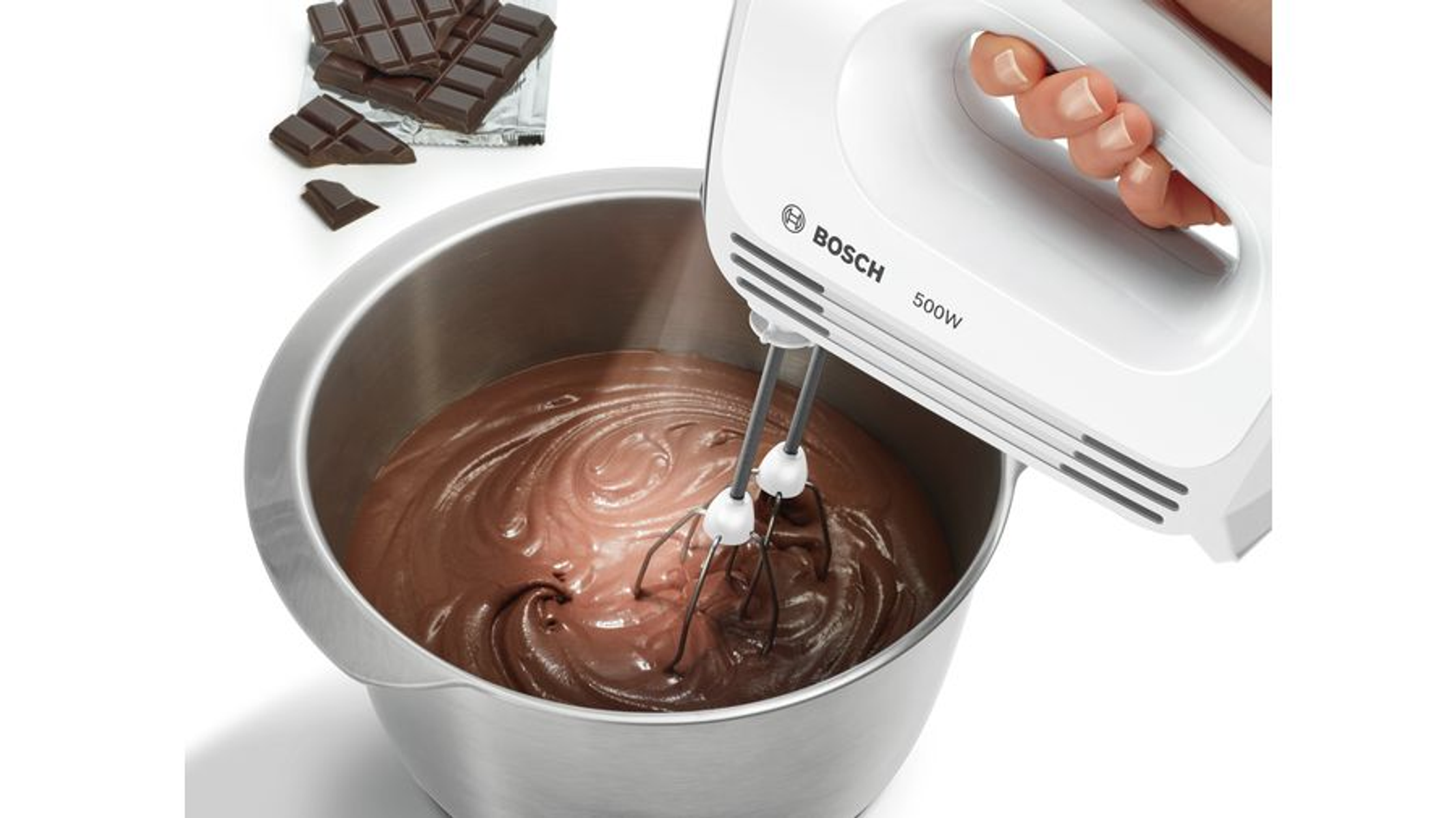Hand verwendet Bosch-Mixer, um Schokoladenteig in einer Schüssel zu verrühren. Schokoriegel liegen daneben.