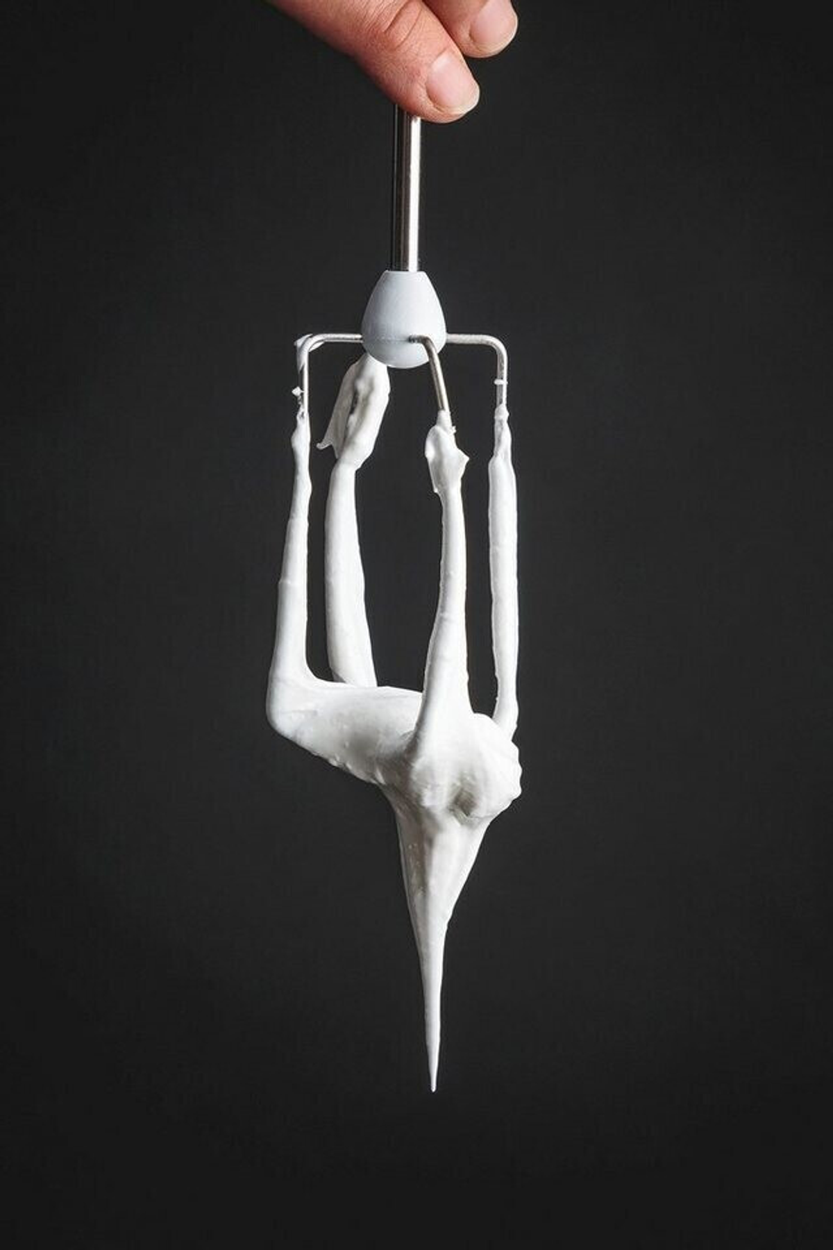Batidor con crema batida, sostenido por una mano, sobre fondo oscuro.