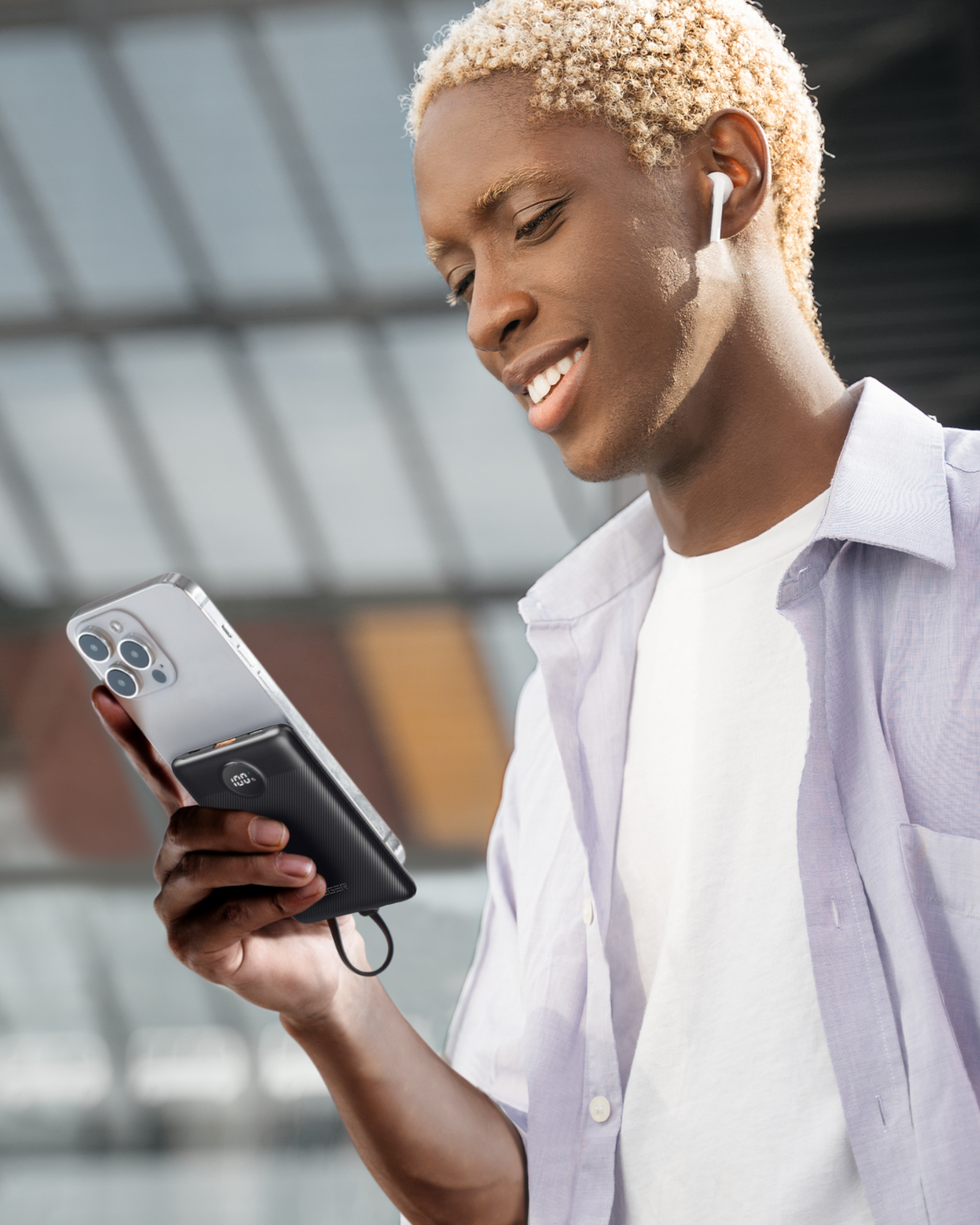 Ein junger Mann, der ein Telefon mit angeschlossener Powerbank hält und draußen lächelt.