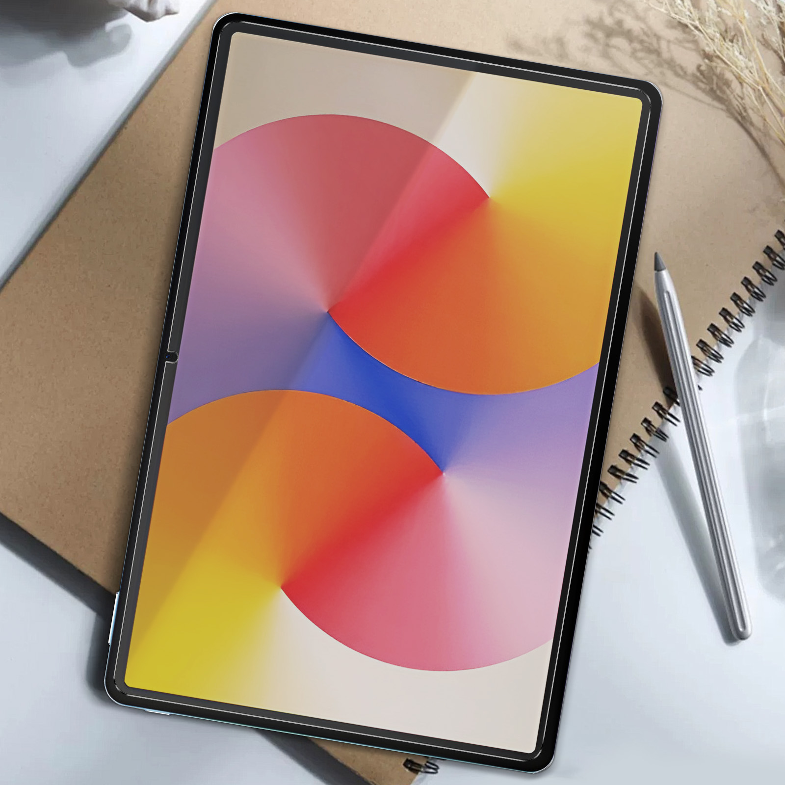 Un tablet con un display colorato, appoggiato su un tavolo con un taccuino e una penna.
