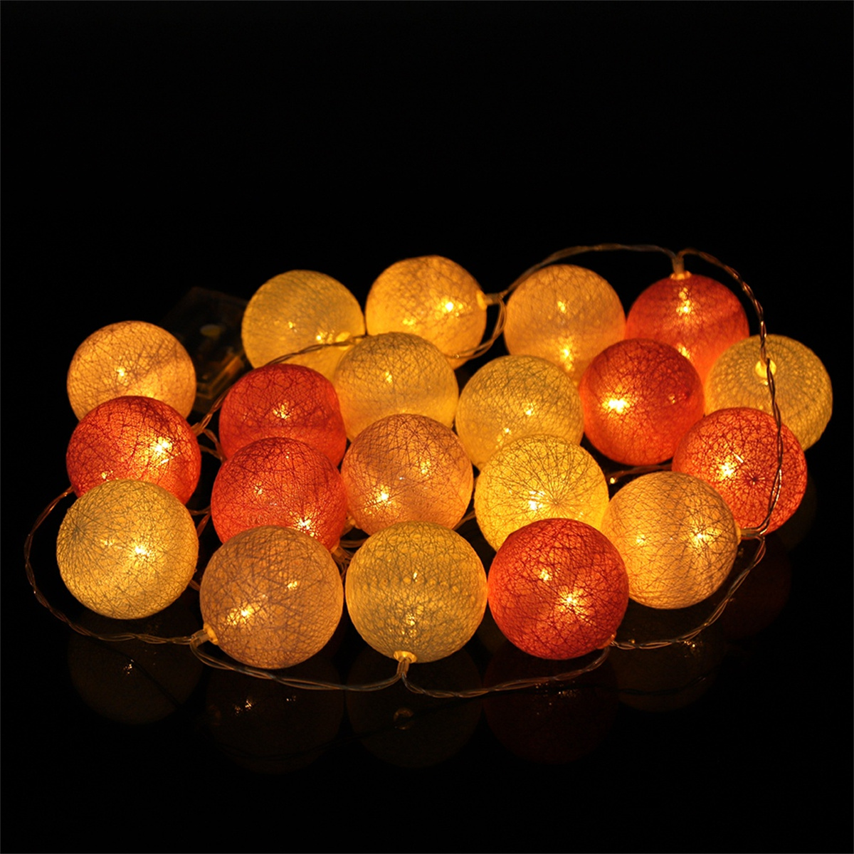 Ein Cluster aus orangefarbenen und gelben Lichterketten. Sie sind kugelförmig und spiegeln sich auf einer schwarzen Oberfläche.