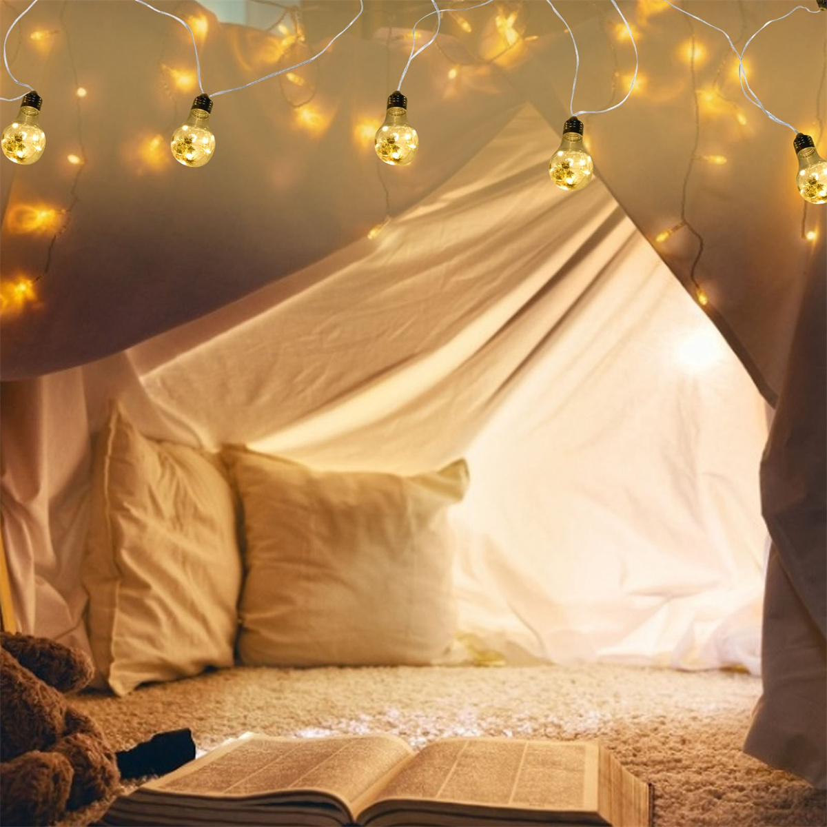 Ein gemütliches Indoor-Fort mit Lichtern, Kissen und einem offenen Buch auf einem Teppich.