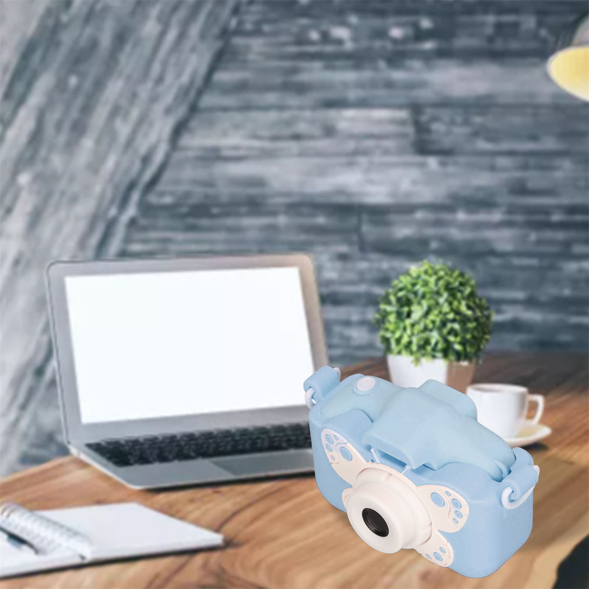 Eine blaue Spielzeugkamera auf einem Holztisch, mit Laptop, kleiner Pflanze und Kaffeetasse.